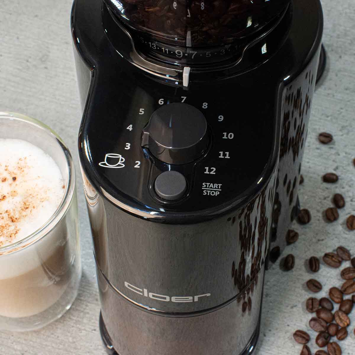 Schwarzer Kaffeemühle mit Einstellung und Tasse Cappuccino daneben.