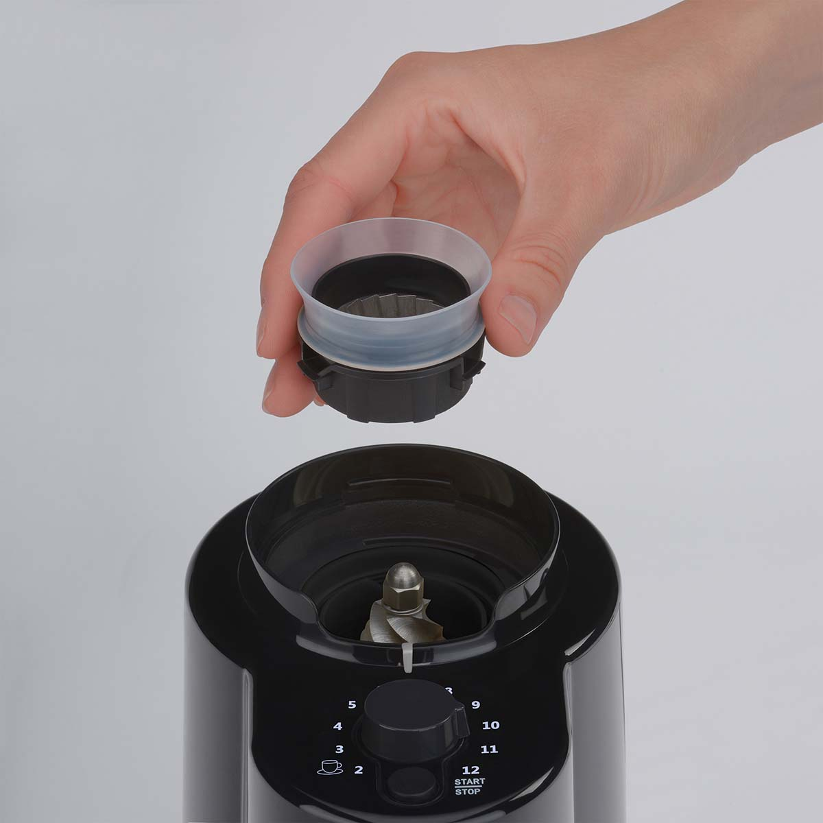 Eine Hand hält einen Mahlwerkaufsatz über einem Kaffeemühlenbehälter.
