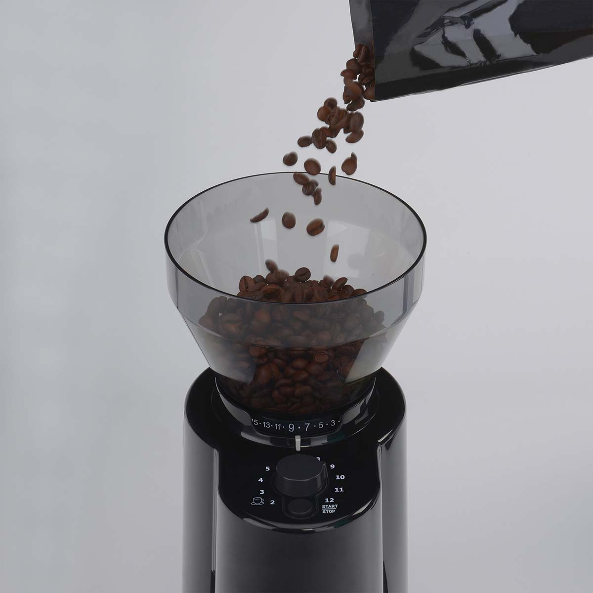 Kaffeebohnen fallen aus einer Packung in einen Kaffeemühlenbehälter.