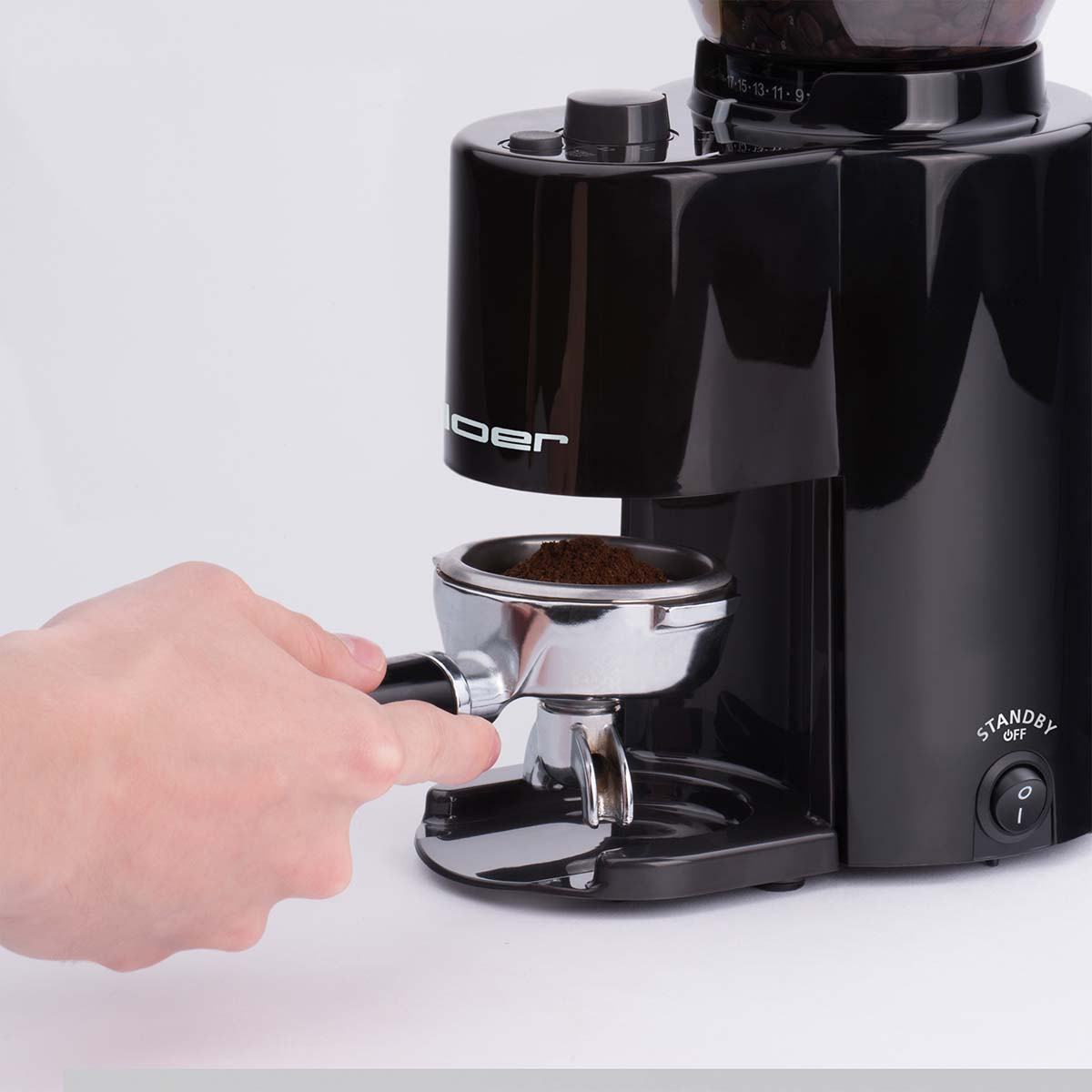 Eine Hand hält einen Siebträger unter eine Kaffeemühle, gefüllt mit Kaffeepulver.
