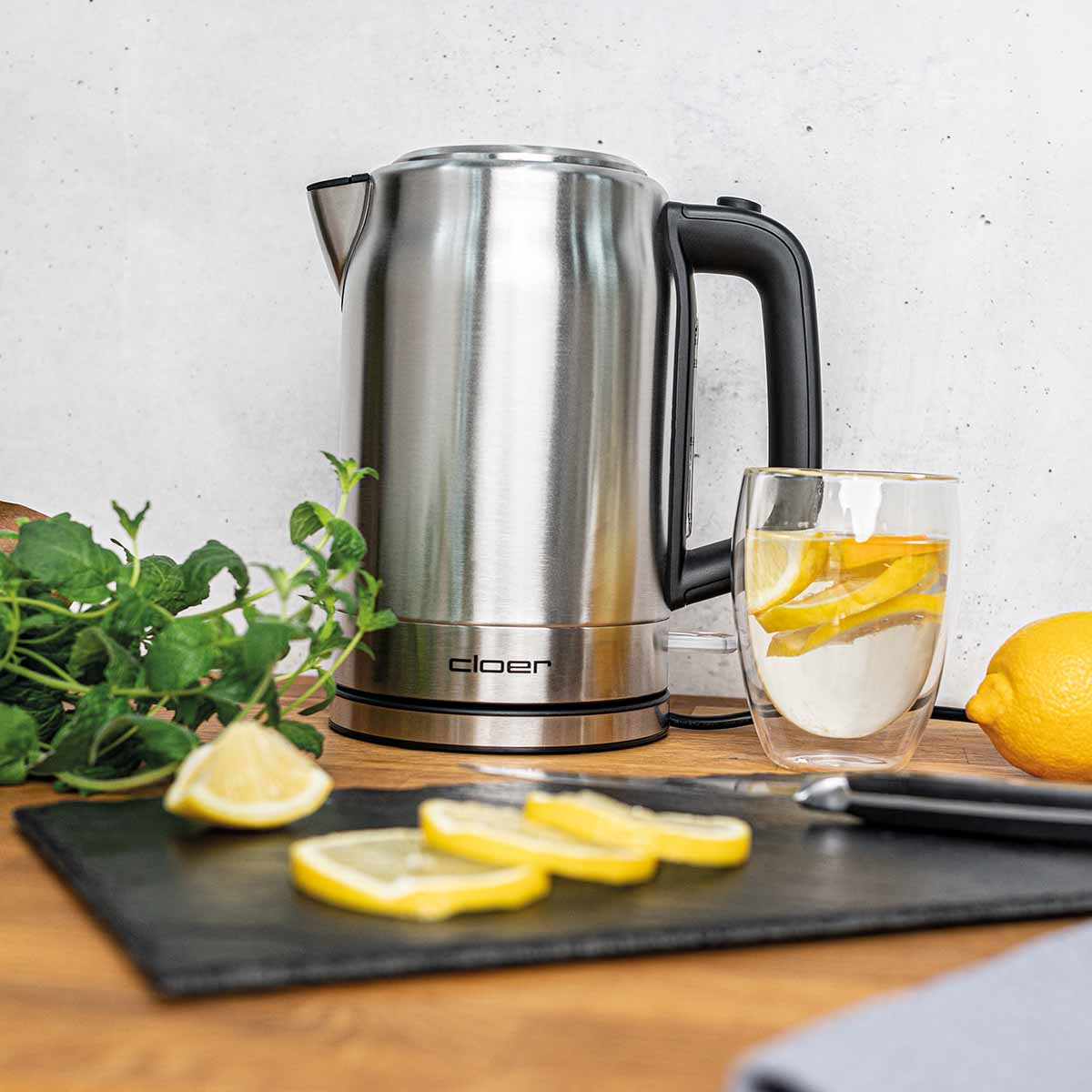 Srebrny czajnik obok szklanki wody z cytryną i miętą.