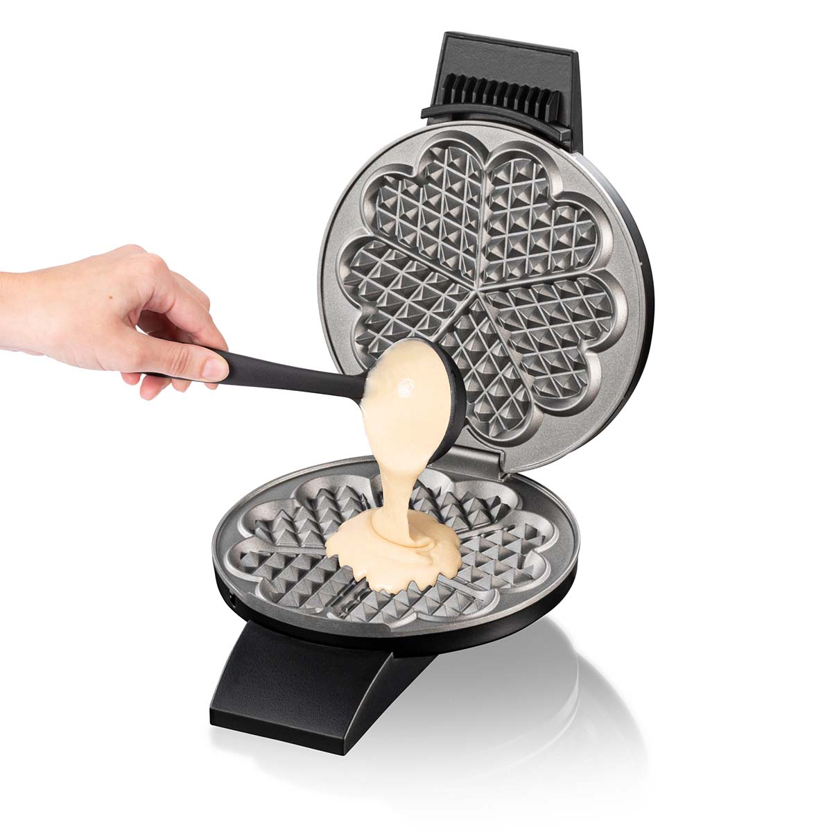 Ręka wylewa ciasto z chochli do gofrownicy w kształcie serca.