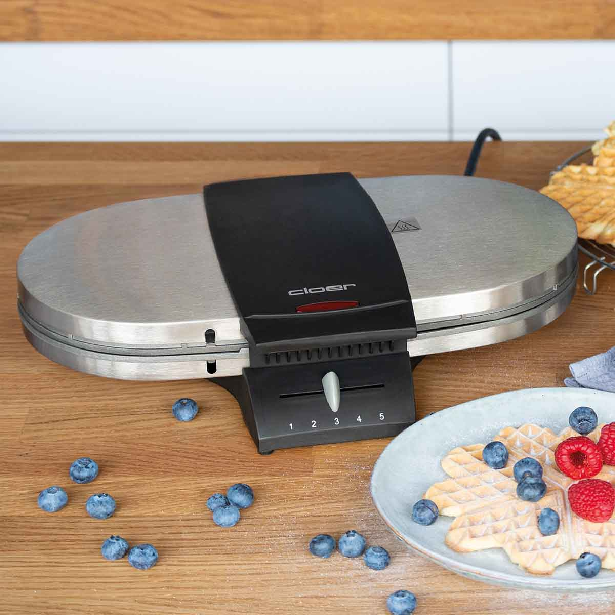 Srebrna gofrownica na drewnianym stole z jagodami i goframi.