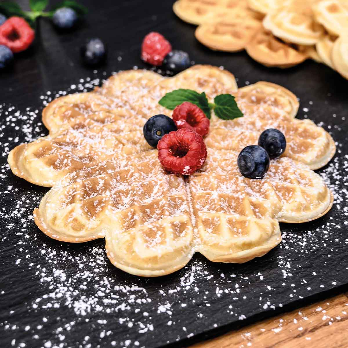 Gofry w kształcie kwiatka z cukrem pudrem, jagodami i miętą.