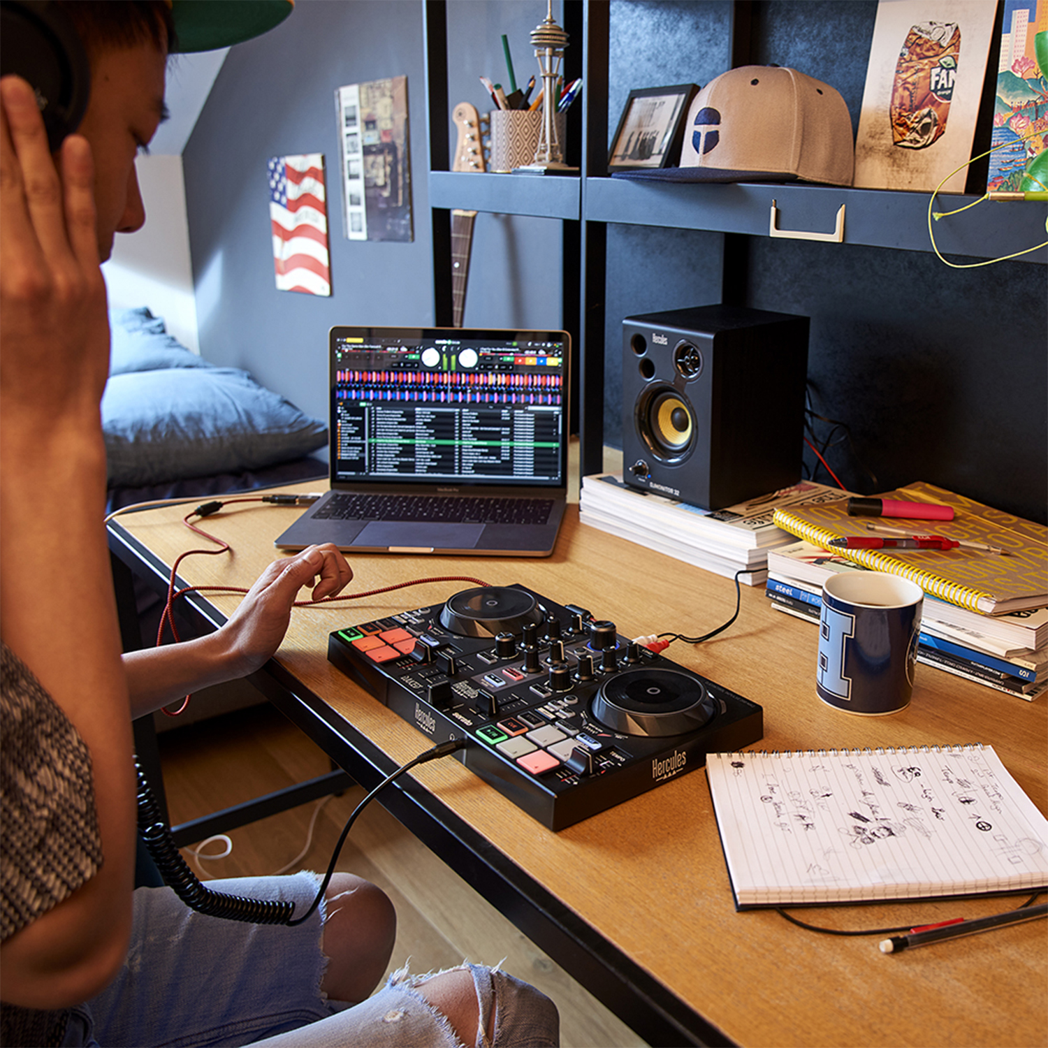Un joven con auriculares usa un controlador DJ frente a una laptop y un altavoz.