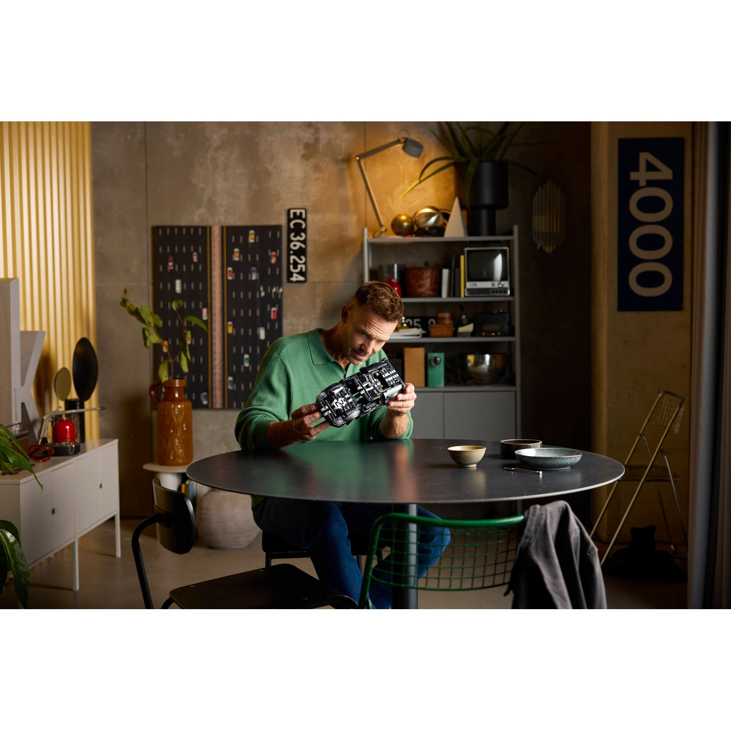 Mężczyzna w zielonym swetrze siedzi przy stole, trzymając model techniczny.