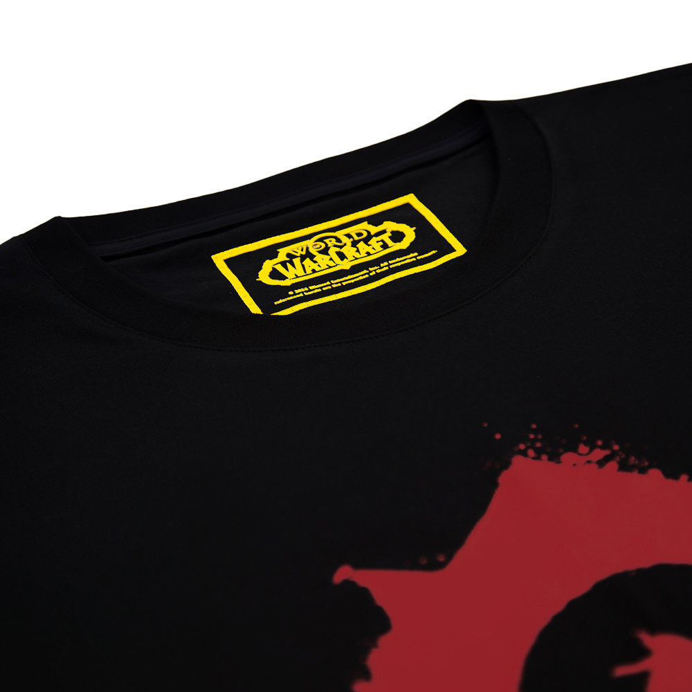 Schwarzes T-Shirt mit gelbem Warcraft-Logo-Etikett und rotem Farbspritzer-Design.