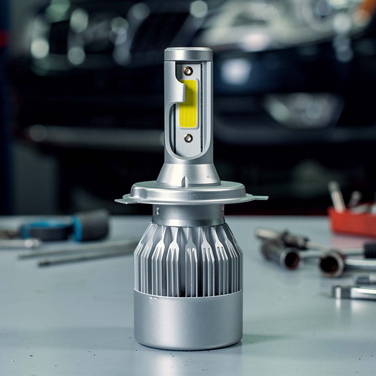 Eine silberne LED-Autolampe mit Kühlrippen, Werkzeug und dunklem Auto im Hintergrund.