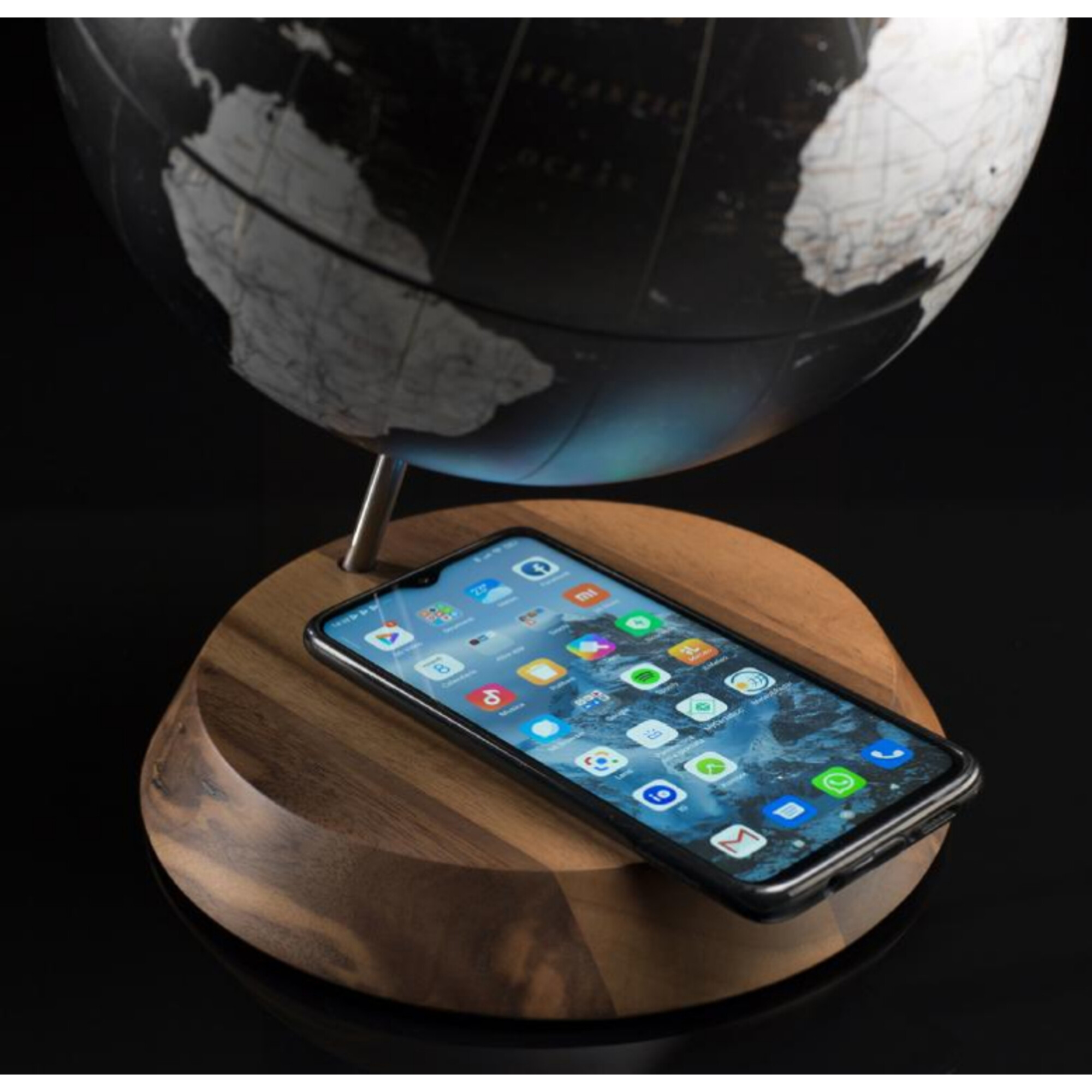 Ein Smartphone liegt auf einem Holzsockel unter einer Weltkugel.
