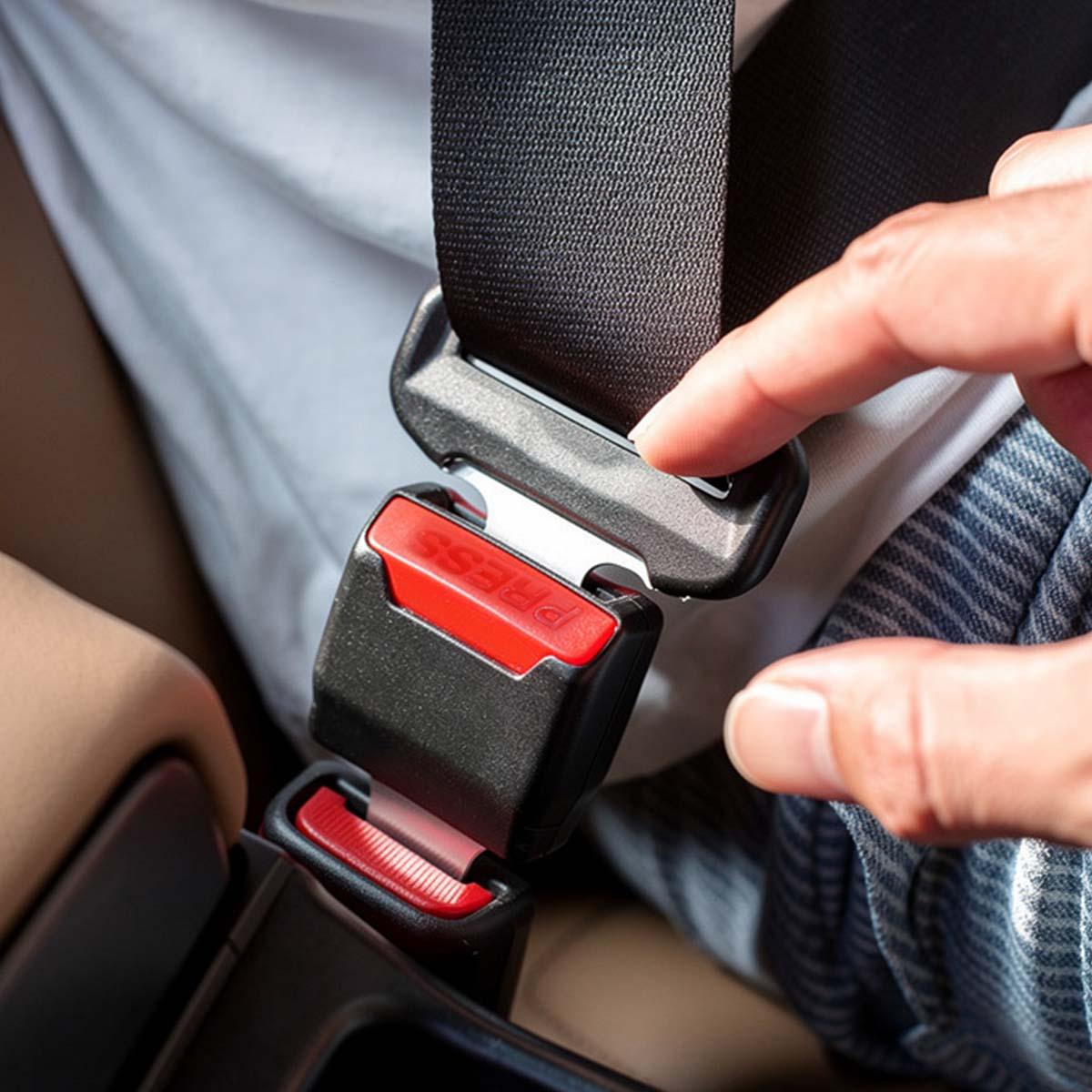 Ein Finger drückt auf den roten Knopf des Auto-Sicherheitsgurtschlosses.