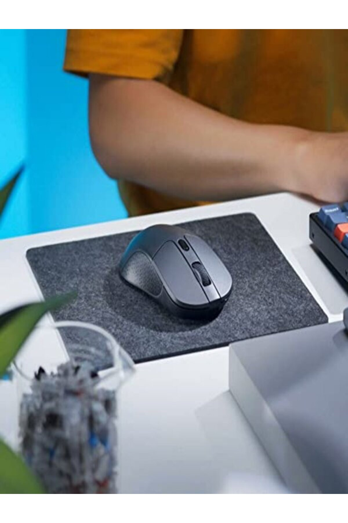 Szara mysz na filcowej podkładce, osoba w żółtej koszulce w tle.