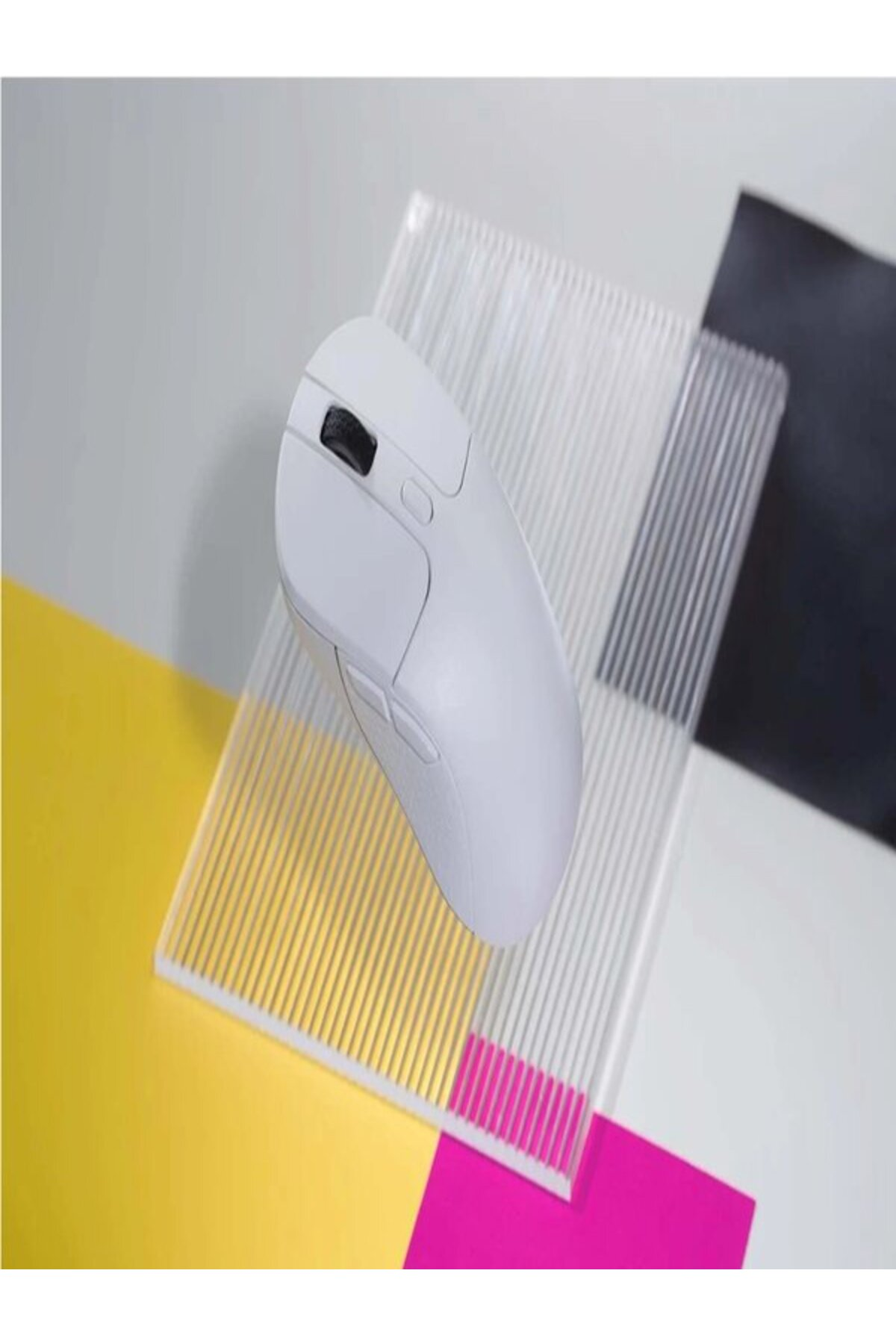 Biała mysz spoczywa na przezroczystej płycie nad kolorowym papierem.