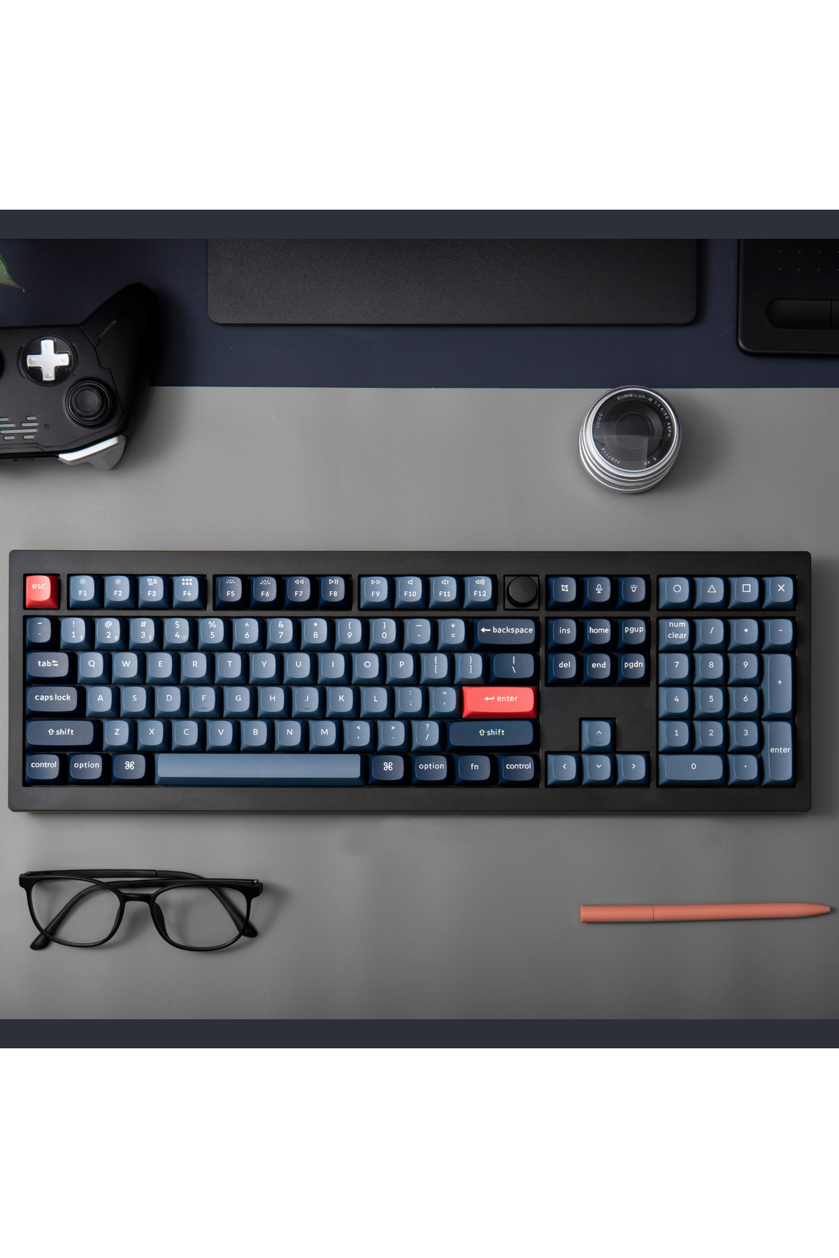 Klawiatura, mysz, kontroler, okulary i długopis na biurku.