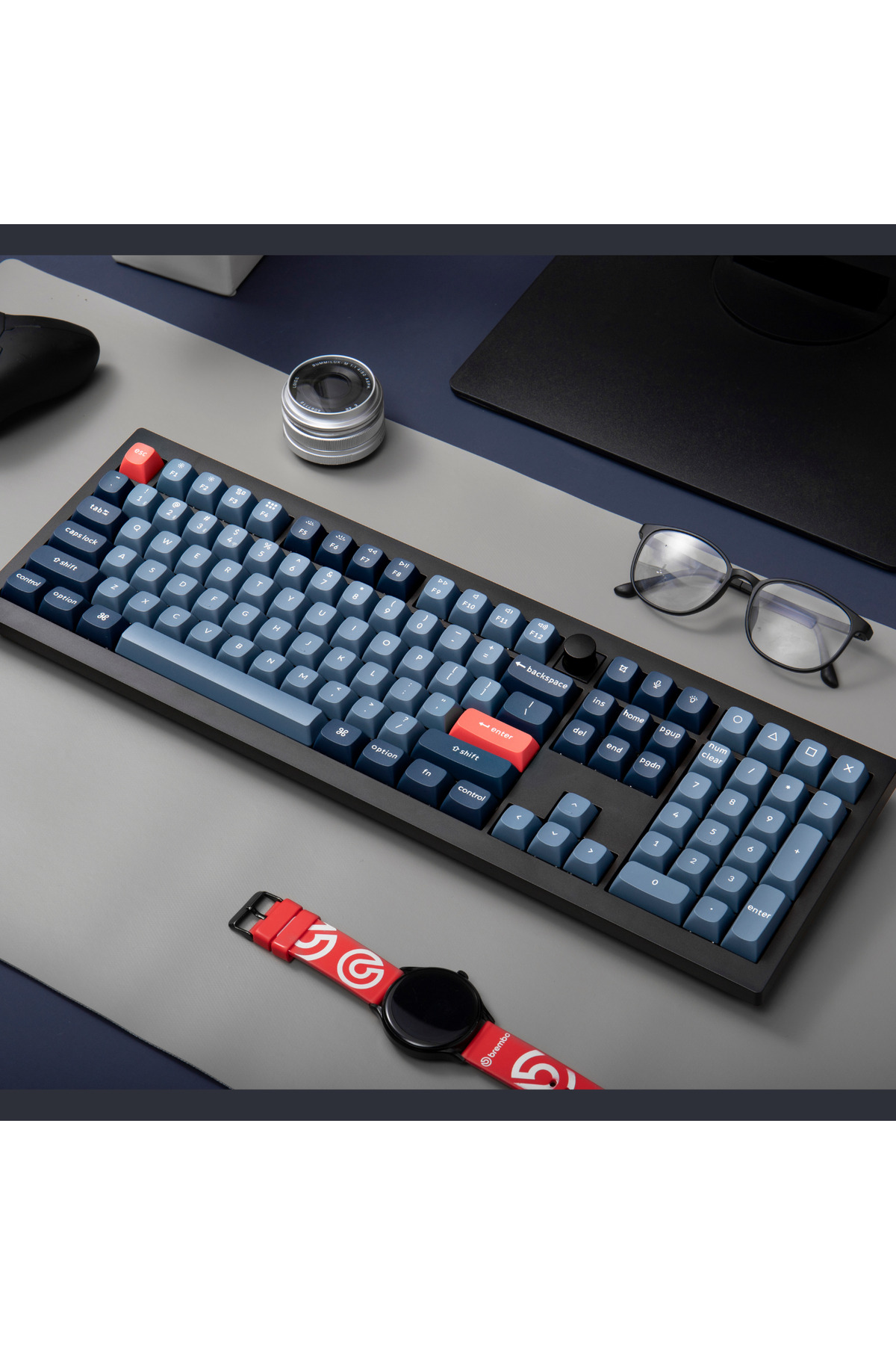 Niebieska klawiatura mechaniczna z czerwonymi klawiszami akcentującymi, okularami.
