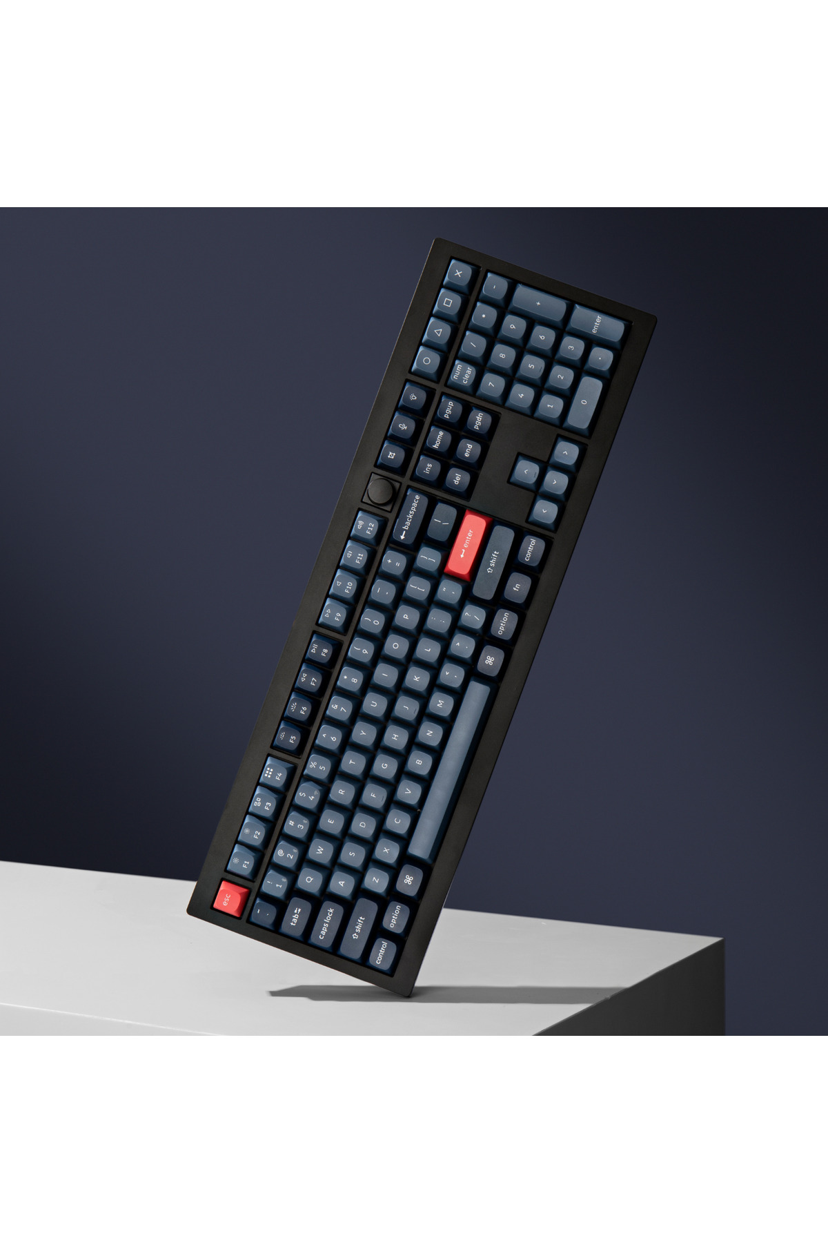 Czarna klawiatura z niebieskimi klawiszami oraz czerwonymi klawiszami Esc i Enter jest ustawiona pod kątem na białej powierzchni.