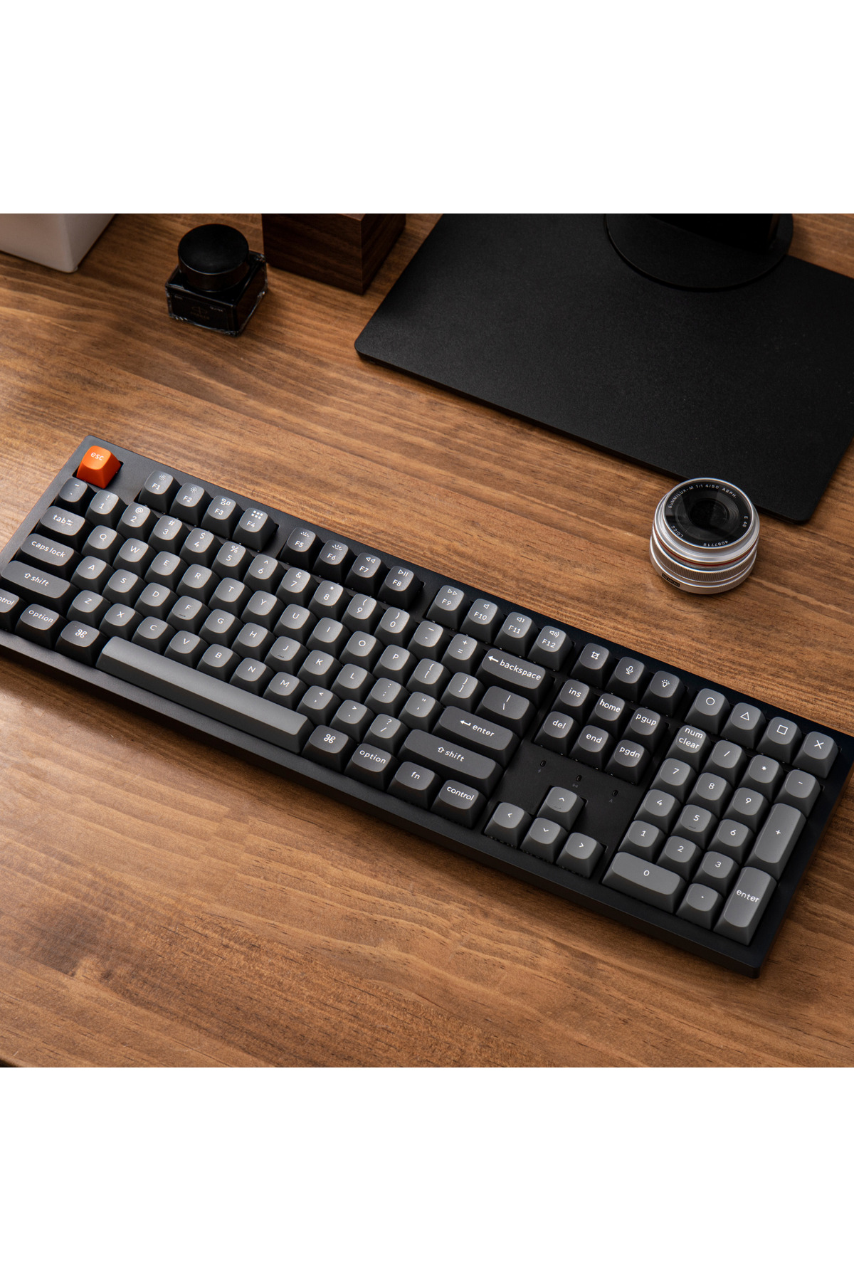 Szara klawiatura z pomarańczowym klawiszem ESC na drewnianym biurku.