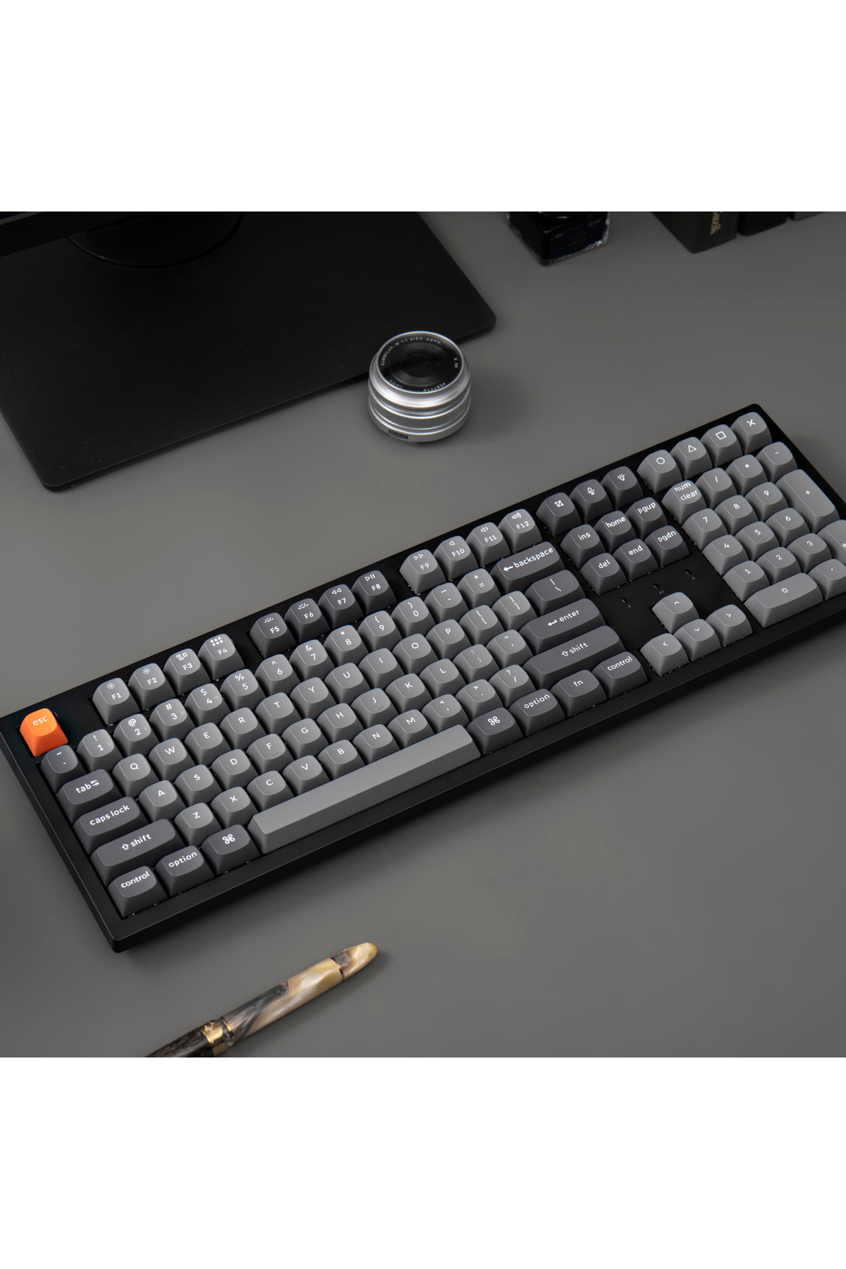 Czarna klawiatura z szarymi klawiszami i pomarańczowym klawiszem ESC. Pióro w pobliżu.