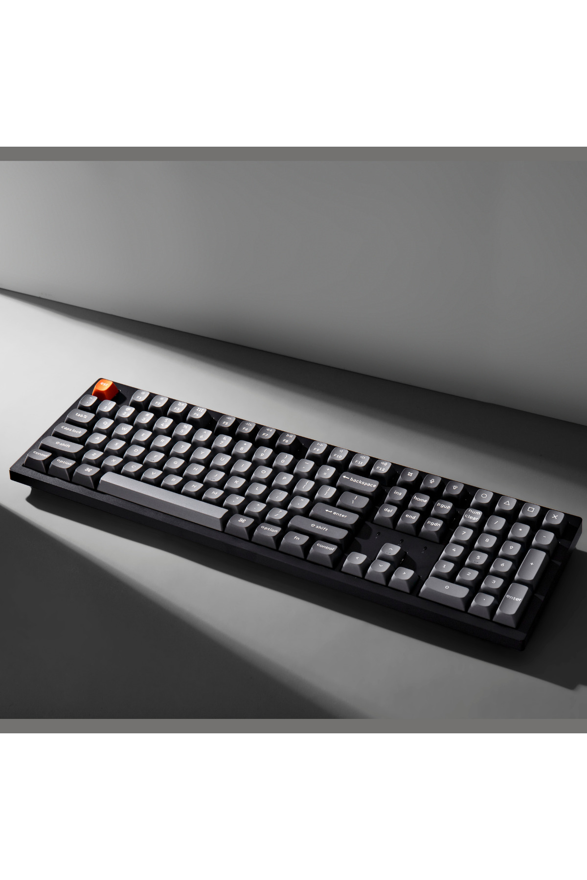 Czarna klawiatura z szarymi klawiszami, pomarańczowy klawisz Esc, na szarej powierzchni.