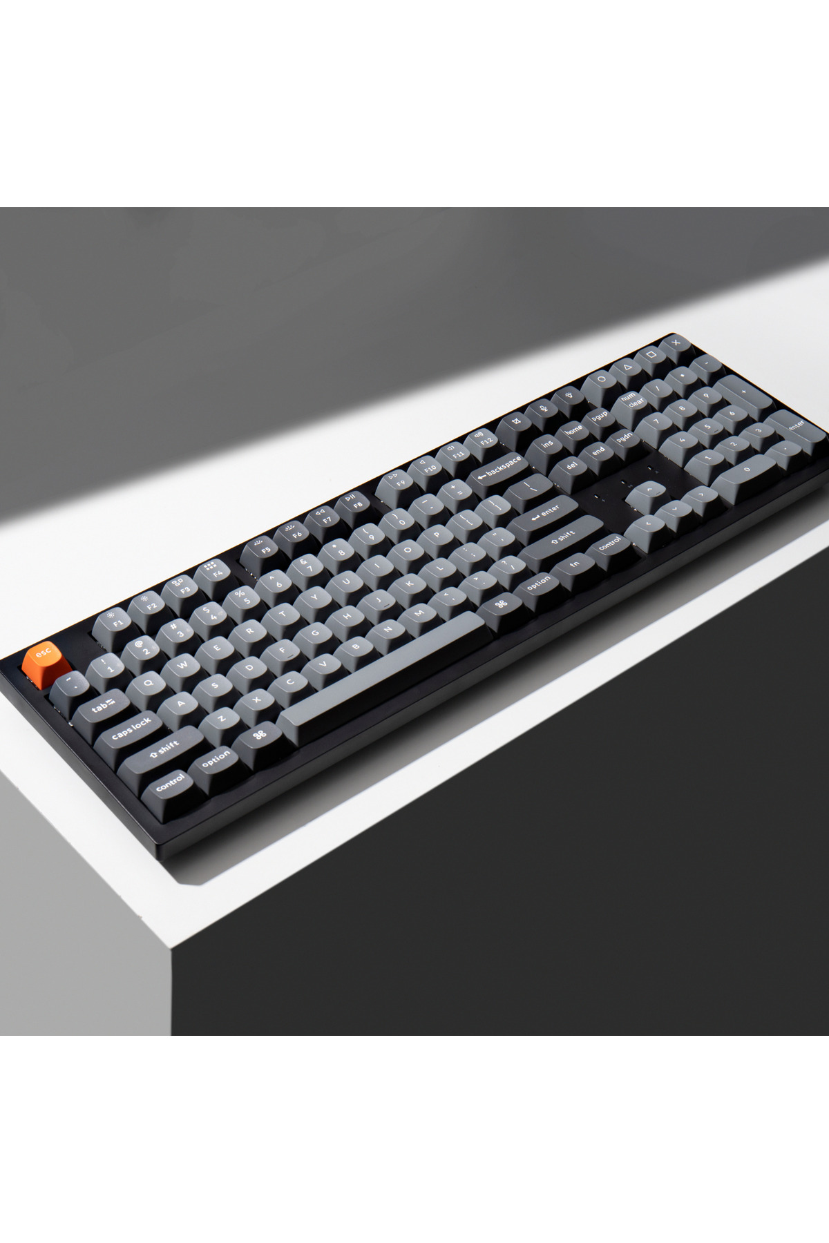 Czarna klawiatura z szarymi klawiszami stoi pod kątem na białej powierzchni.