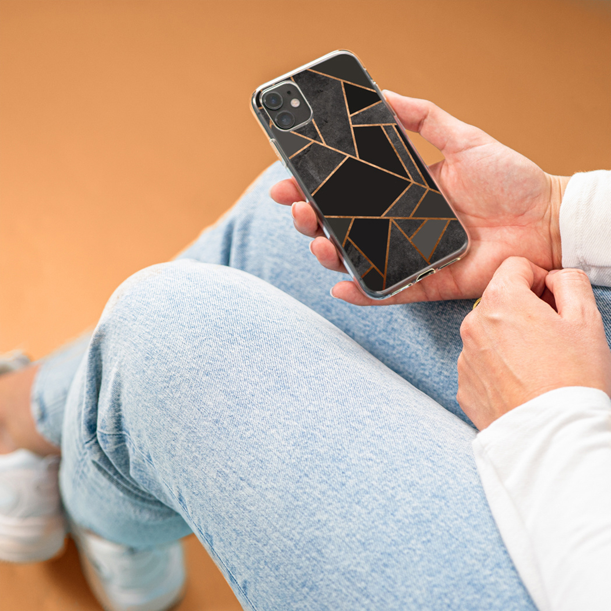 Una mano tiene uno smartphone con motivo marmorizzato nero e linee dorate.