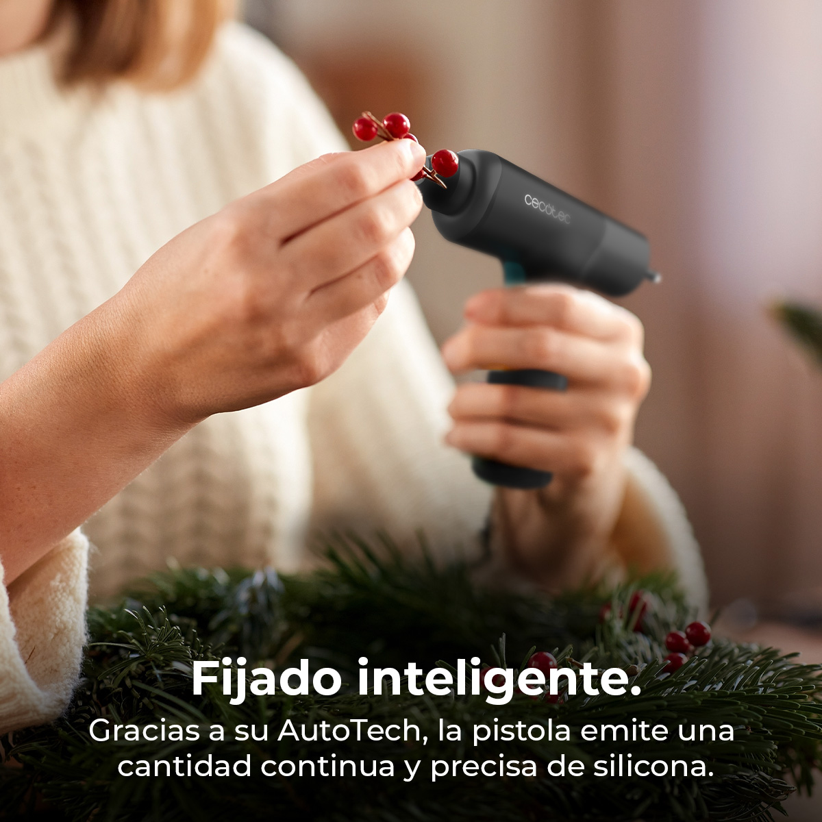 Una persona usa una pistola per colla a caldo per attaccare bacche rosse a una ghirlanda di pino.