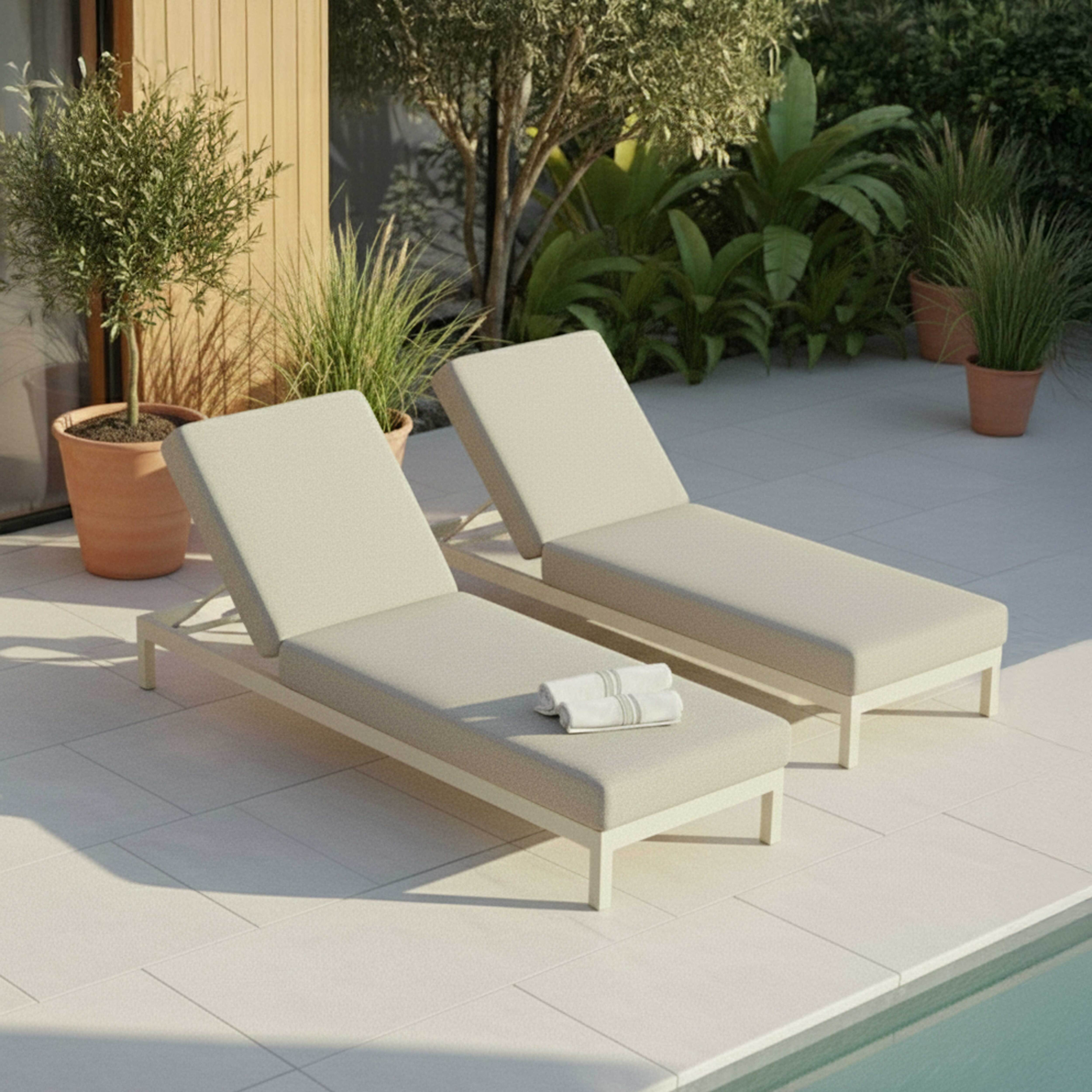 Zwei Liegestühle aus hellem Stoff stehen auf einer gefliesten Terrasse neben einem Pool.