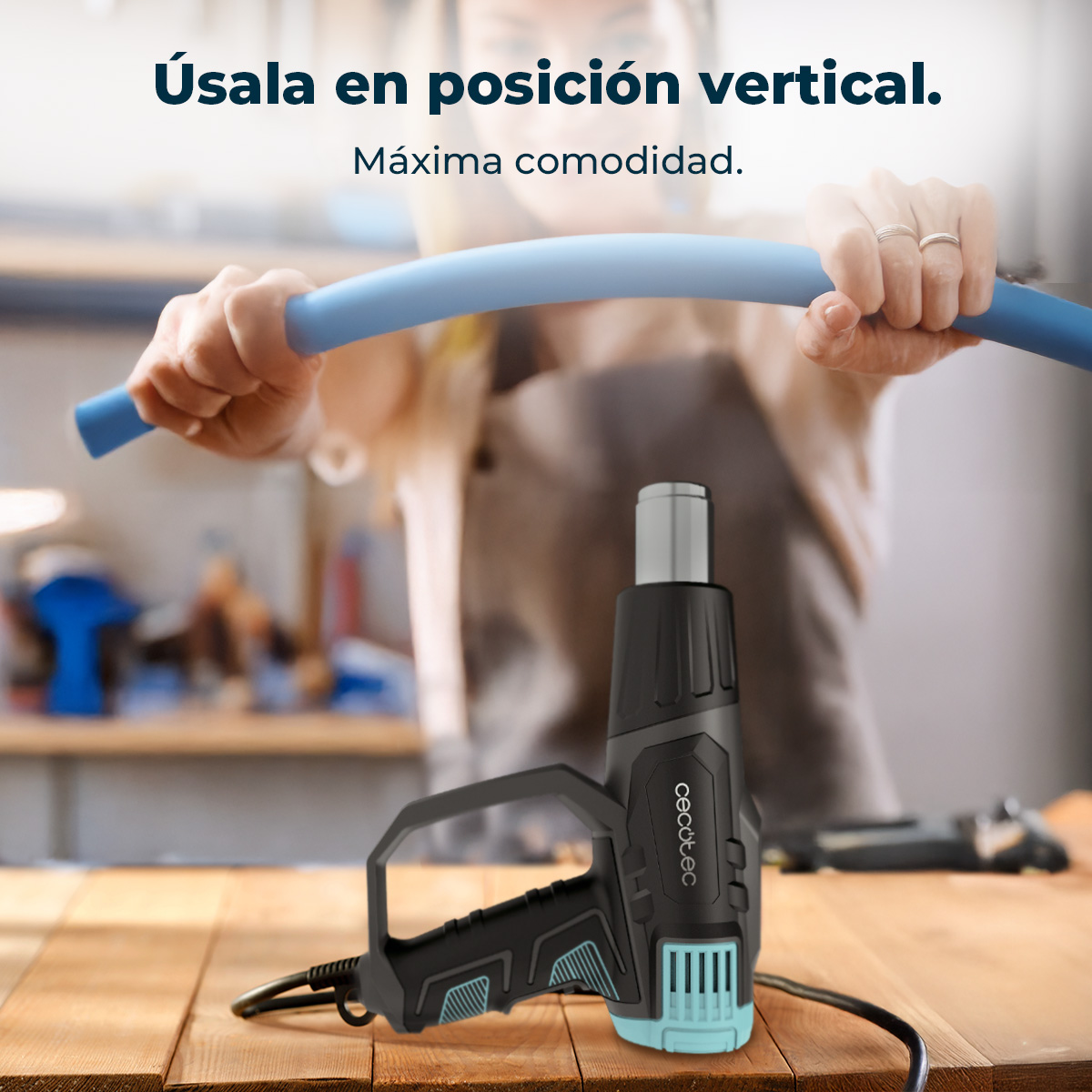 Un secador de aire caliente negro sobre mesa de madera. Manos doblan tubo azul.