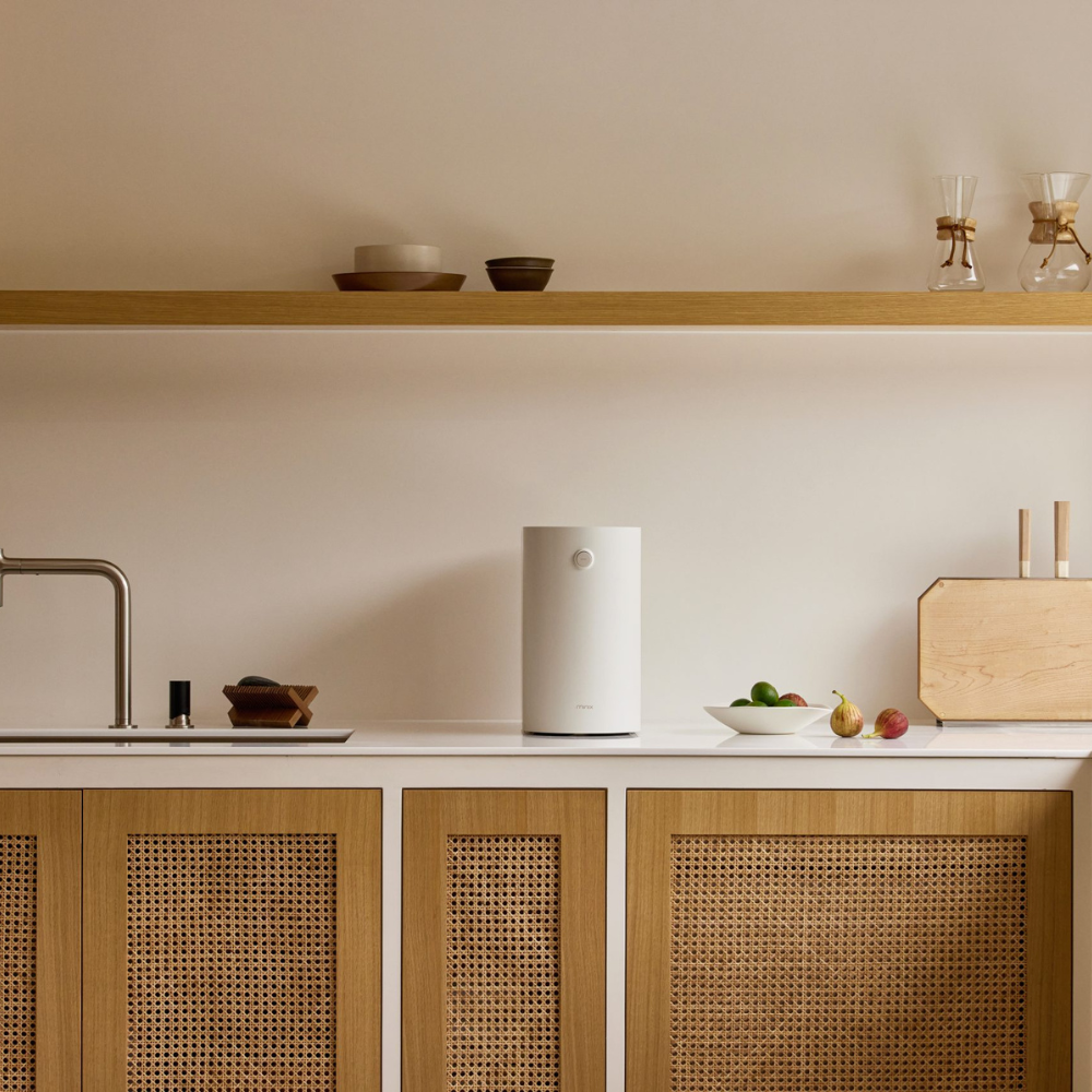 Un purificatore d'aria bianco è sul bancone della cucina accanto a frutta e tagliere di legno.