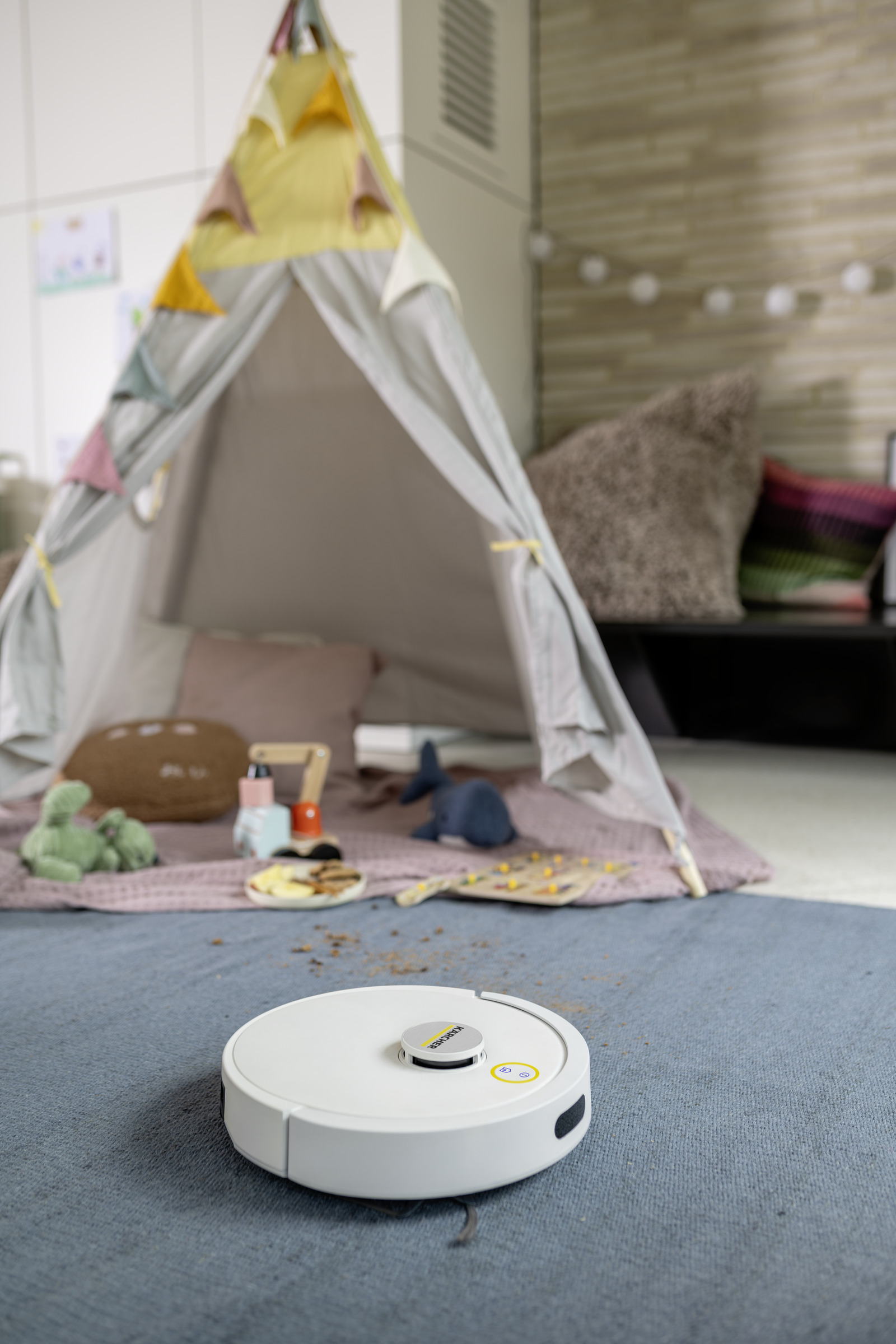 Biały robot sprzątający na niebieskim dywanie przed namiotem do zabawy z zabawkami.