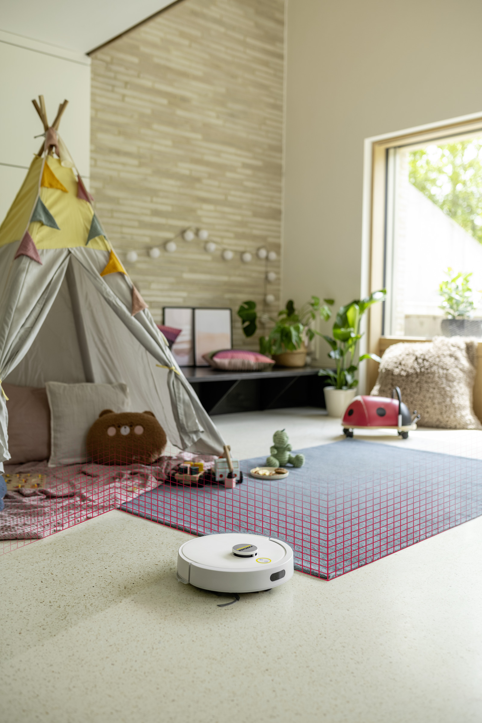 Biały robot sprzątający czyści dywan w pokoju dziecięcym, obok namiotu do zabawy.