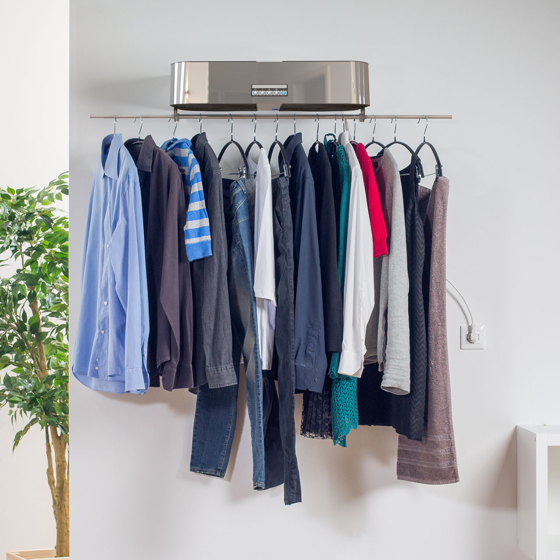 Een kledingrek met kleding hangt aan een muur, met een zilveren apparaat erboven.