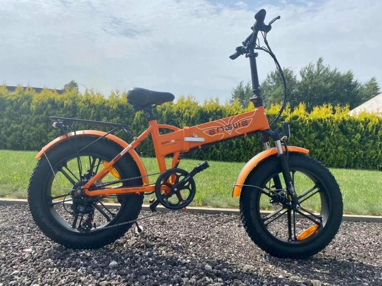 Una bicicletta pieghevole arancione con pneumatici grassi è parcheggiata su ghiaia.