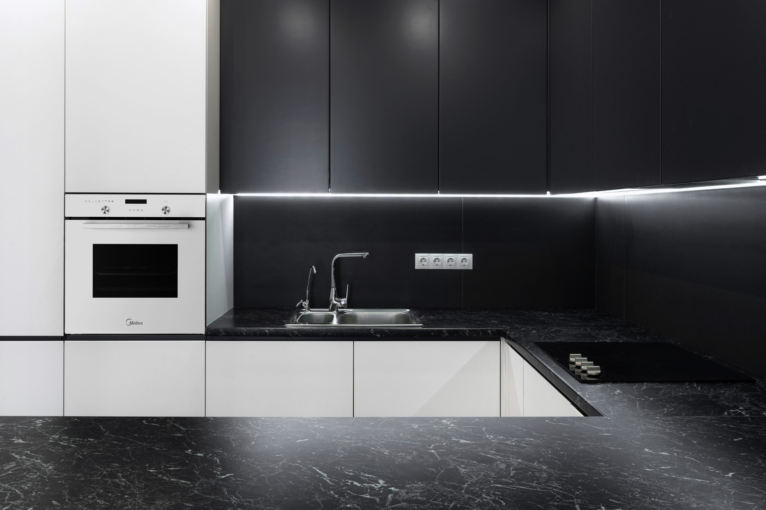 Moderna cocina negra y blanca con horno empotrado, fregadero y vitrocerámica.