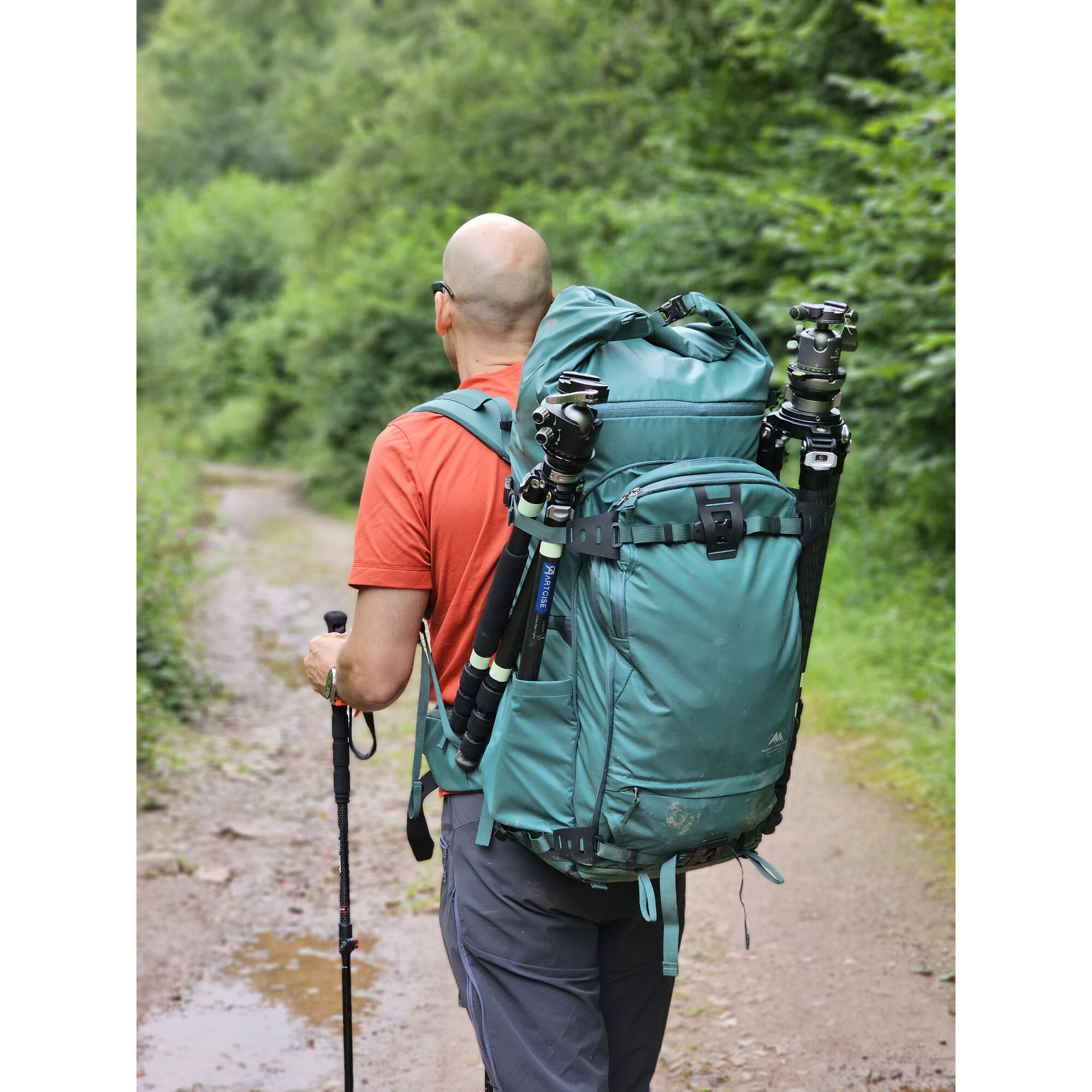 Mann mit Rucksack und Stativ geht auf Waldweg.