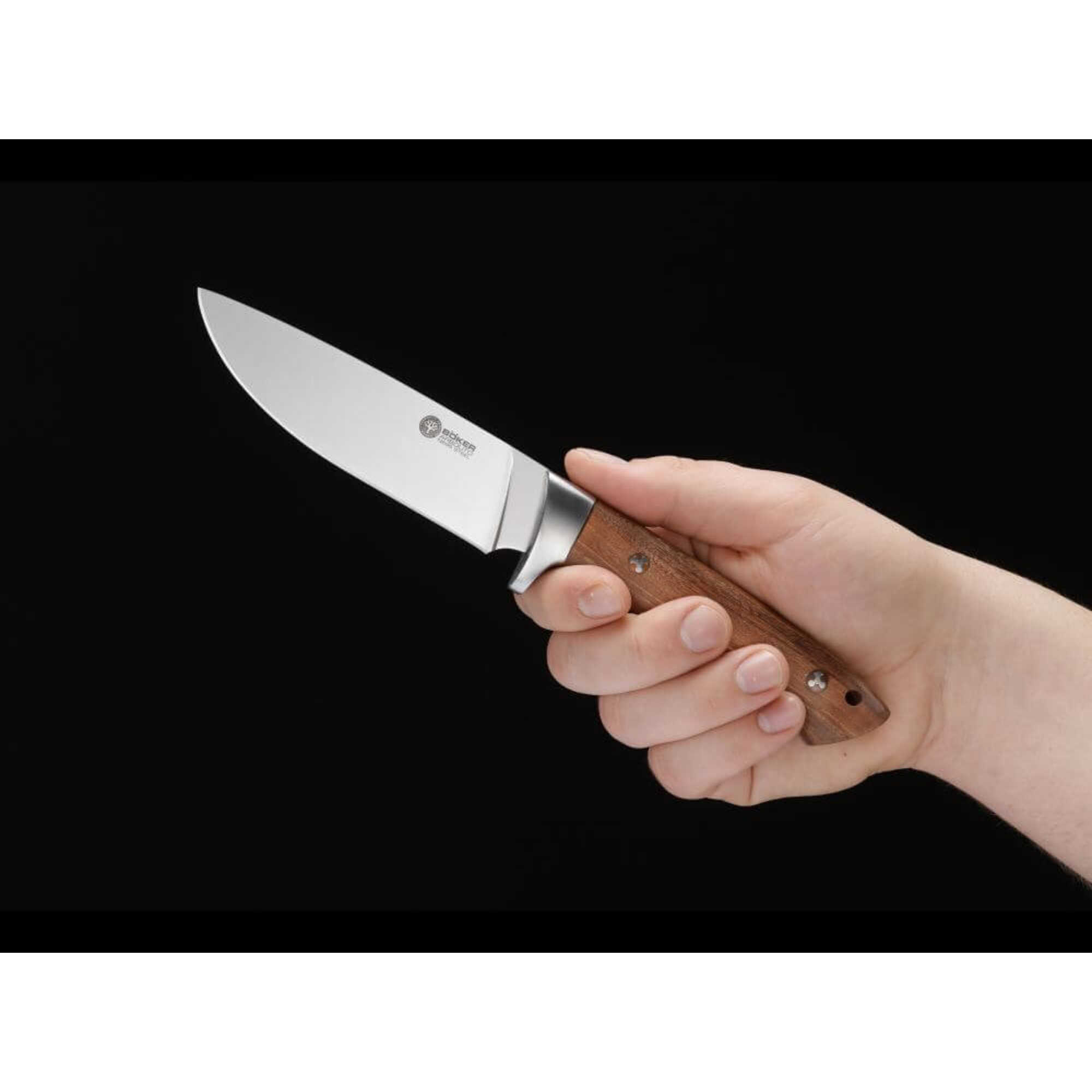 Eine Hand hält ein Messer mit Holzgriff vor schwarzem Hintergrund.