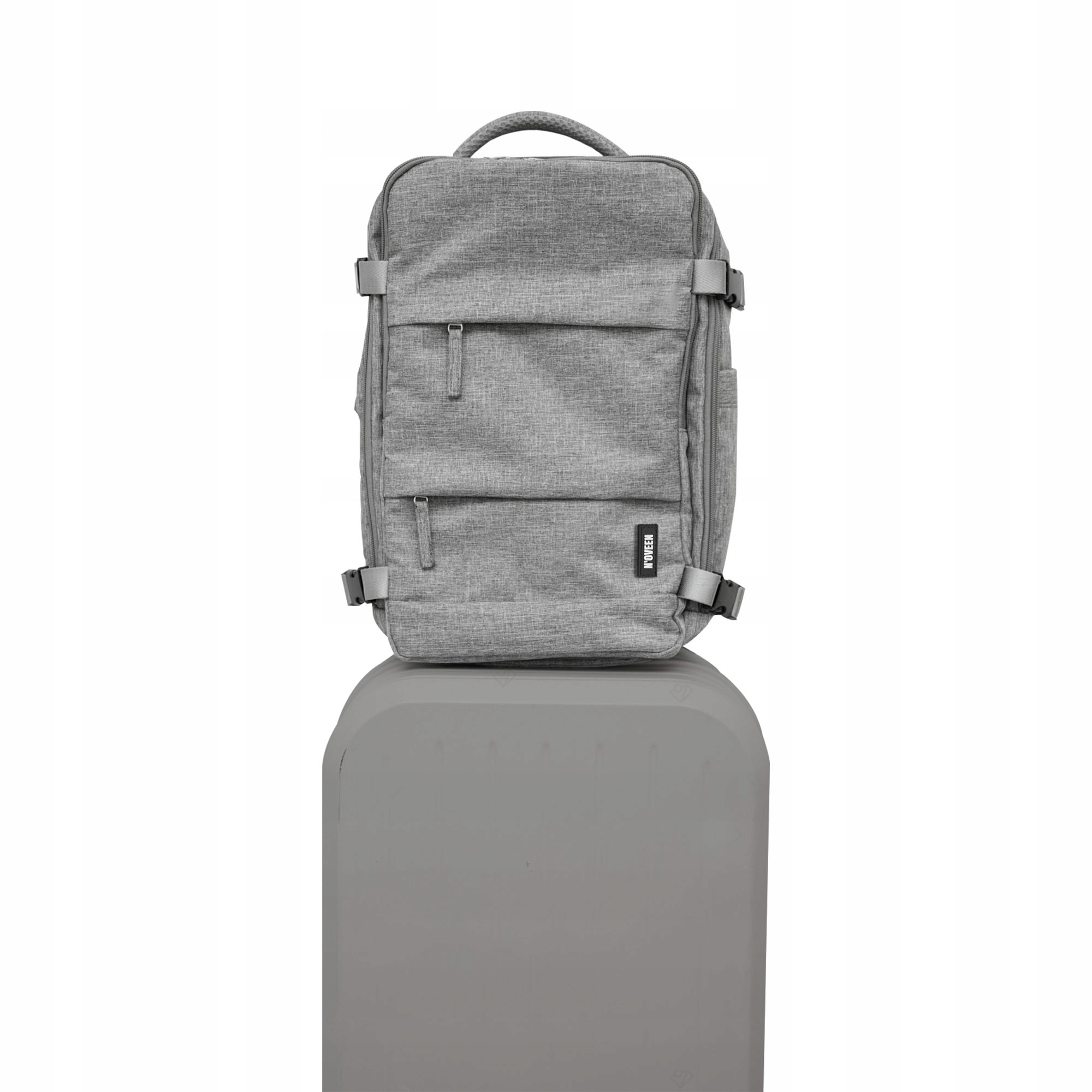 Szary plecak z wieloma przegrodami stoi na szarej podstawie.