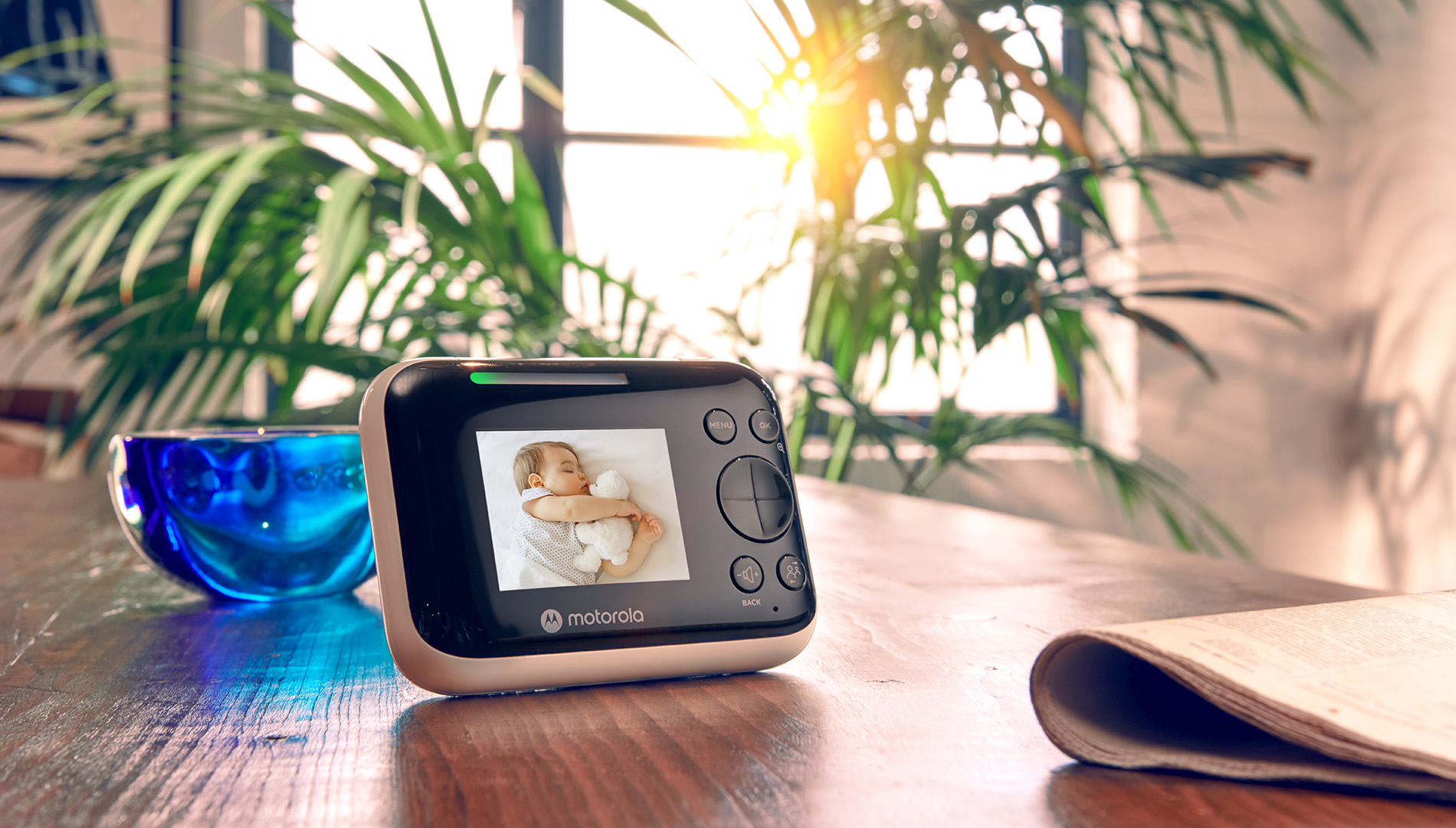 Ein Baby schläft mit einem Teddy auf einem Babyphone. Blaue Schale daneben.