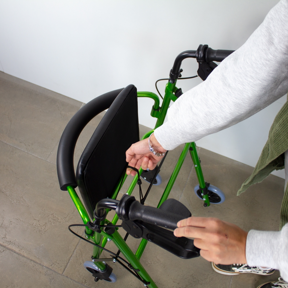 Andador verde con asiento siendo plegado por manos.