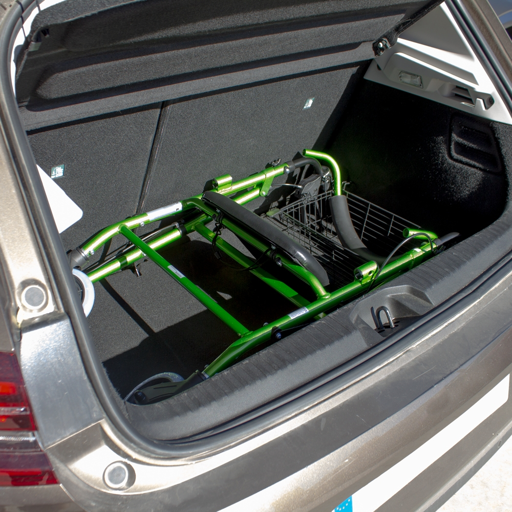 Un andador rollator verde plegado con cesta yace en el maletero de un coche.