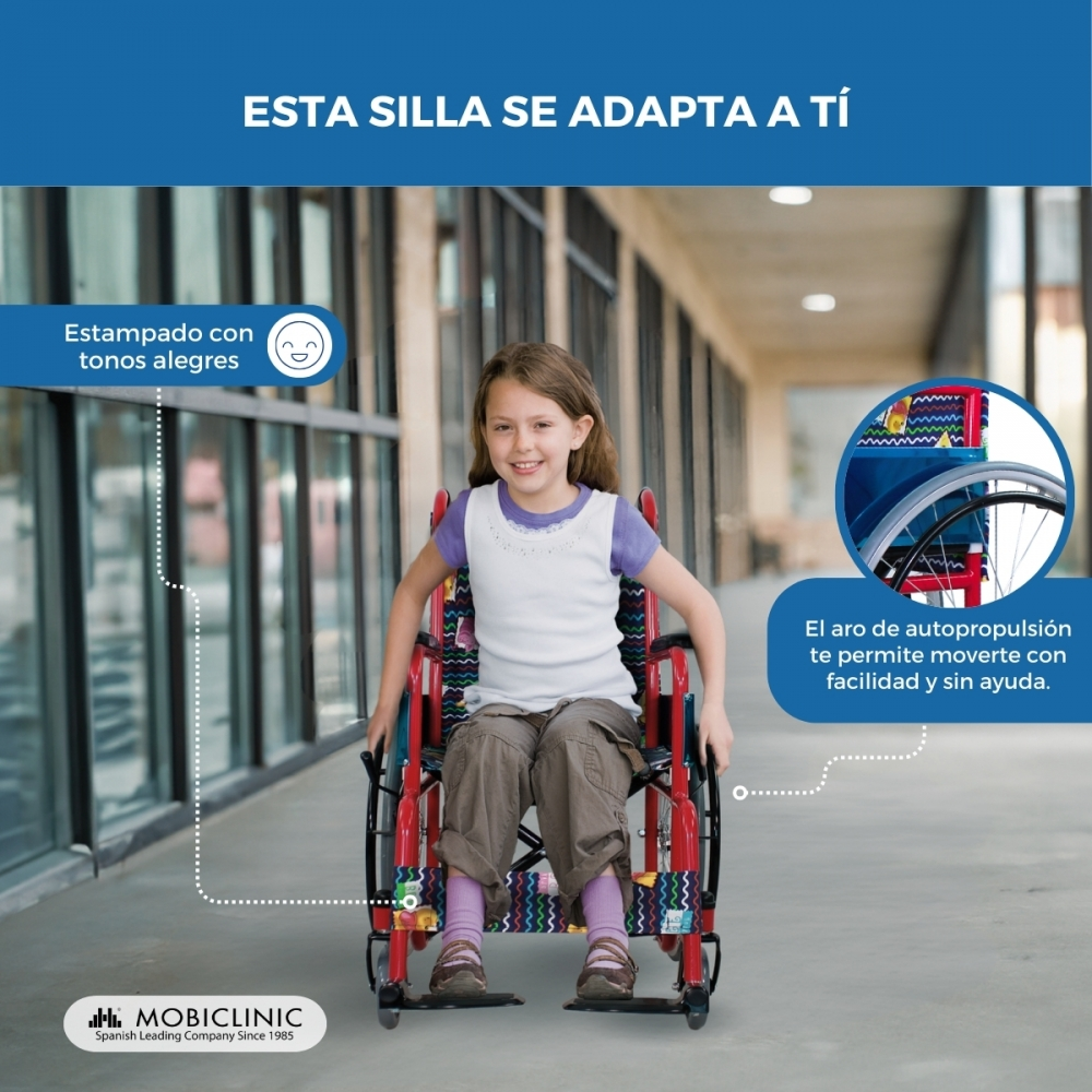 Una niña sonriente en una silla de ruedas colorida en un pasillo.