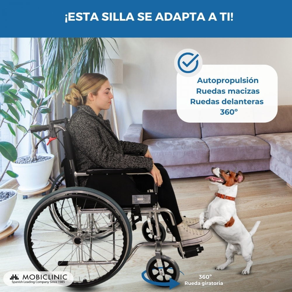 Una mujer sentada en silla de ruedas, un perro delante. Escena interior.