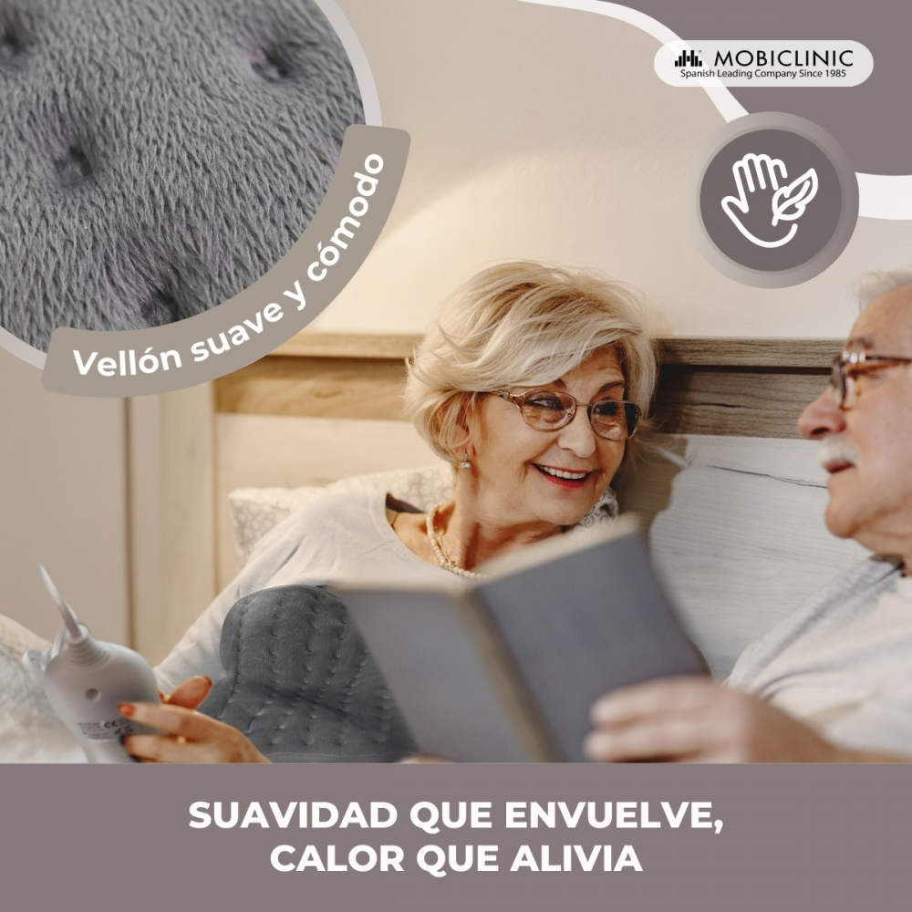 Pareja mayor en la cama leyendo y acurrucándose con una manta gris.