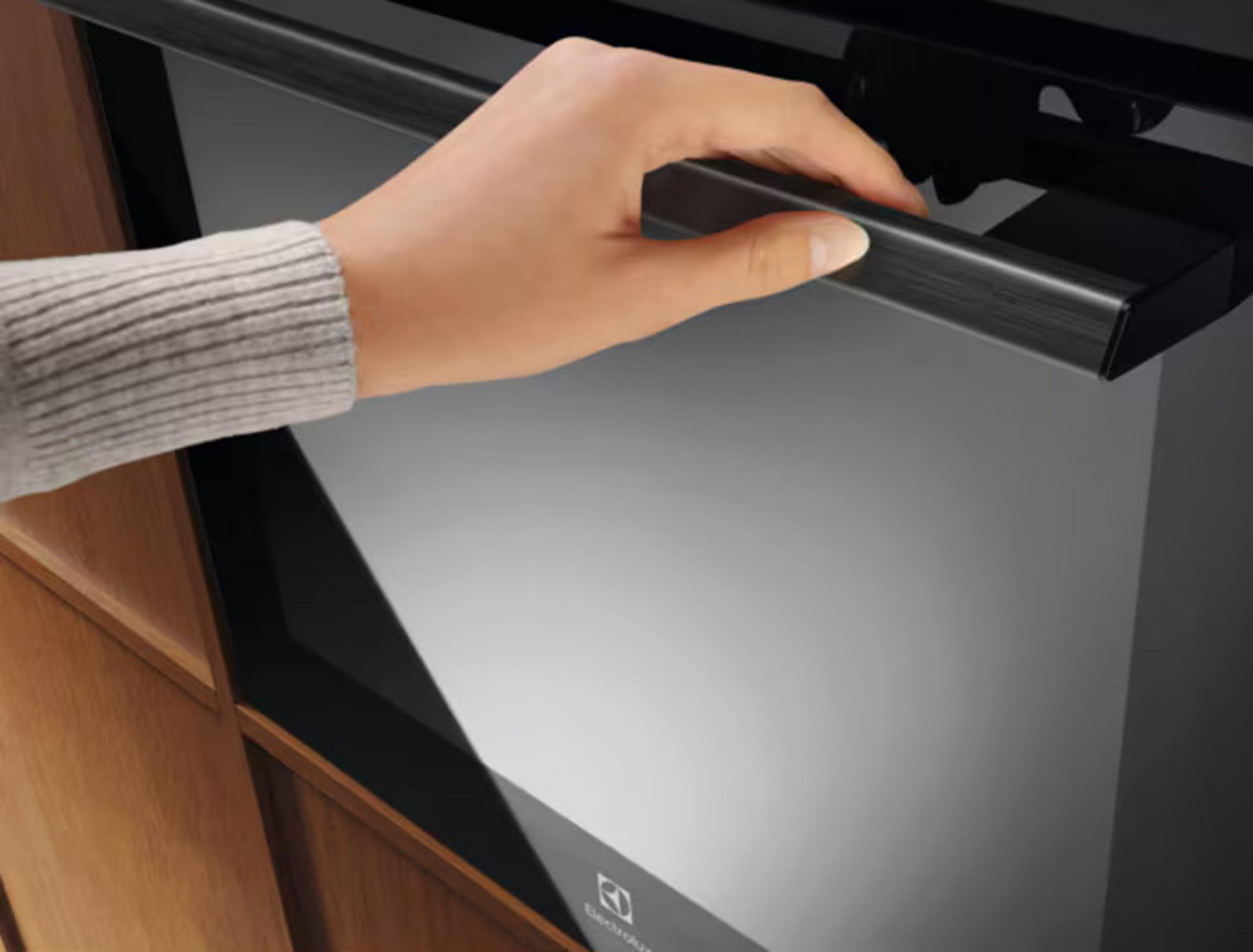Una mano con maglione grigio apre una maniglia del forno nera.