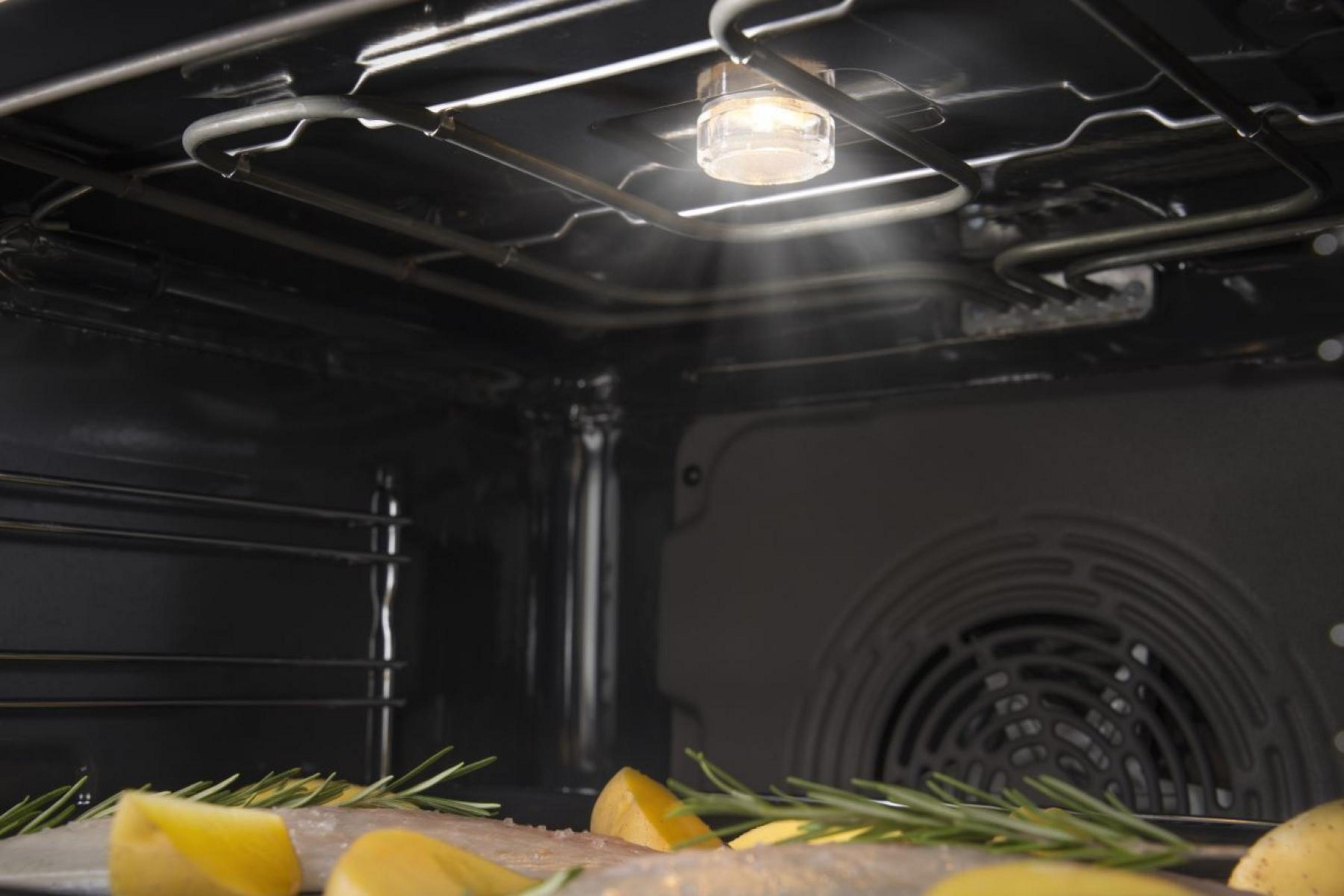 Wnętrze piekarnika z rybą i ziemniakami w trakcie gotowania, oświetlone od wewnątrz.
