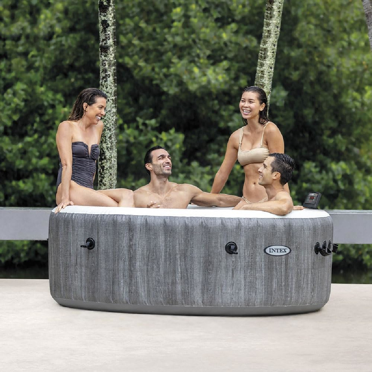 Vier Personen entspannen in einem aufblasbaren Whirlpool im Freien vor grünem Laub.
