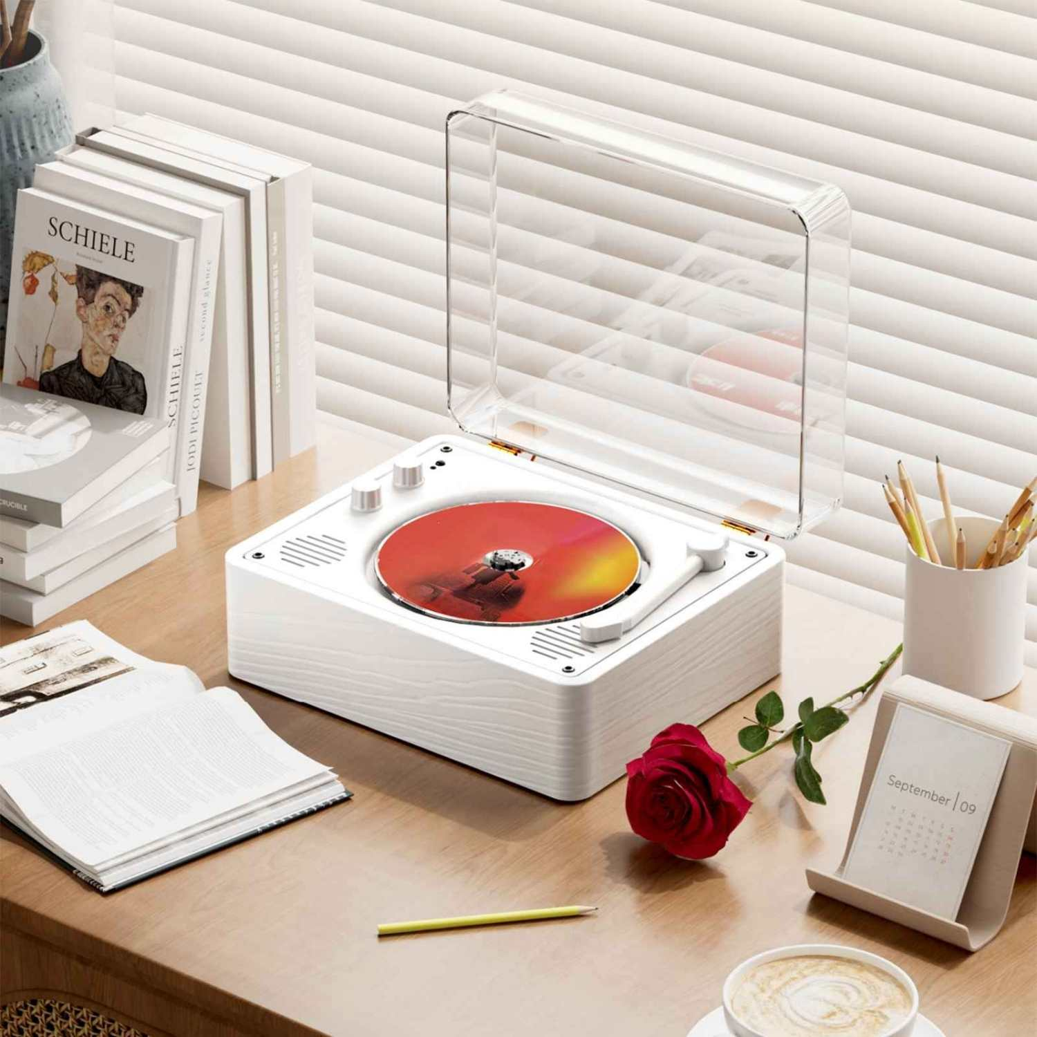 Ein weißer Plattenspieler mit roter CD, Bücher, eine Rose und Kaffee auf einem Schreibtisch.