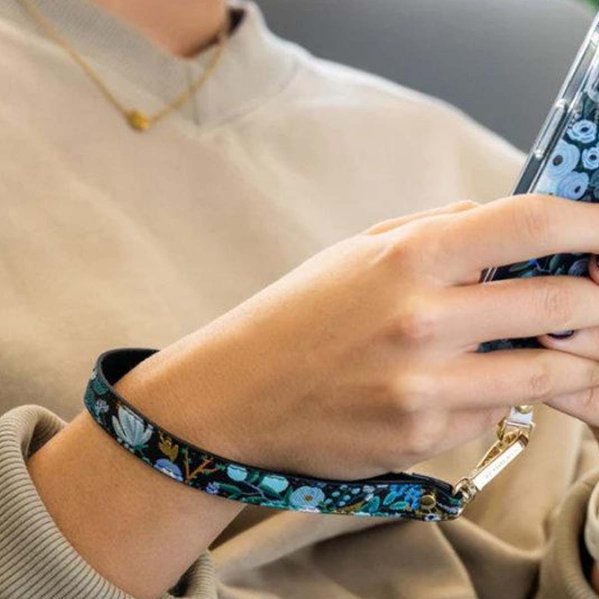 Eine Hand hält ein Handy mit Blumenmuster, eine Handgelenkschlaufe ist angebracht.