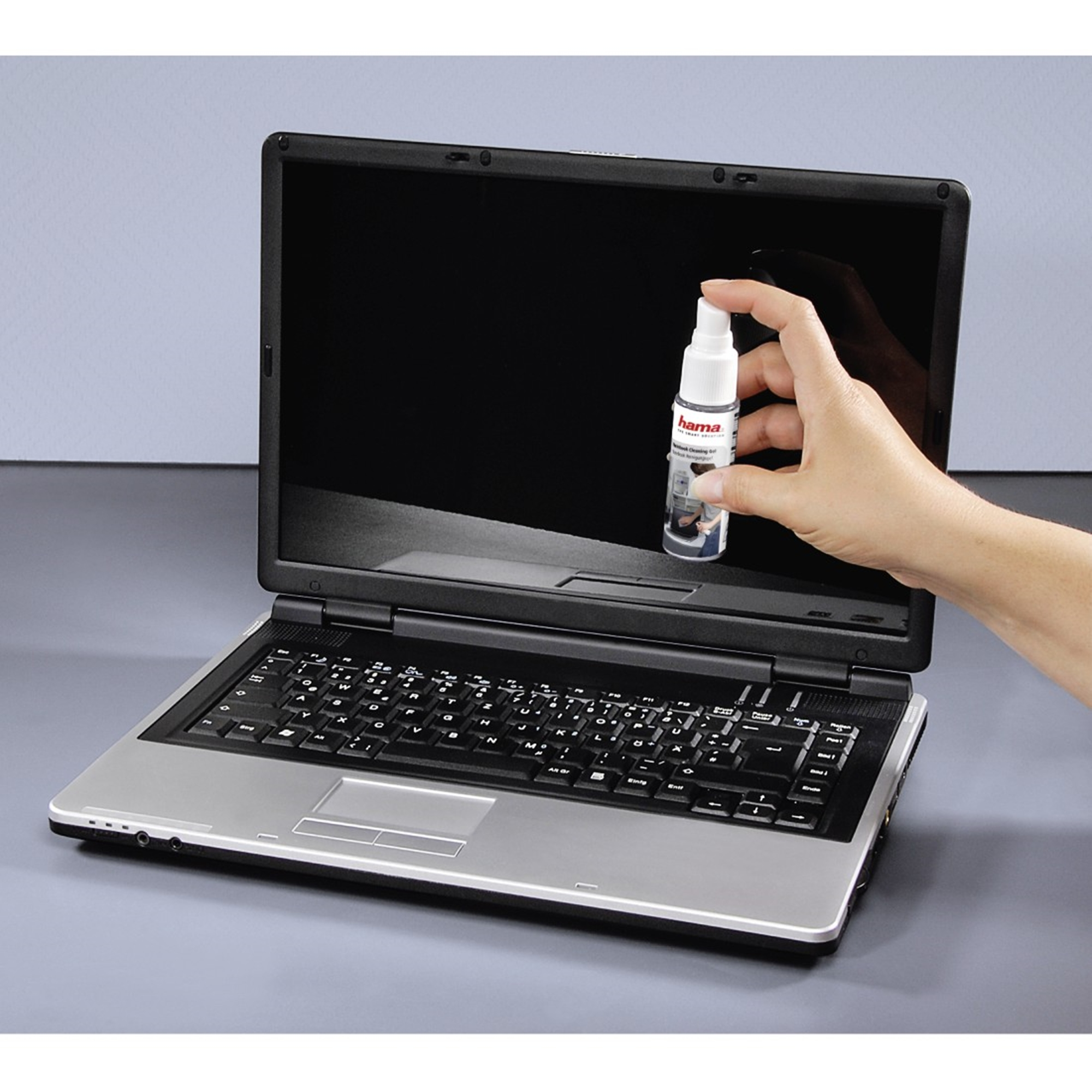 Una mano tiene uno spray sopra un laptop aperto.