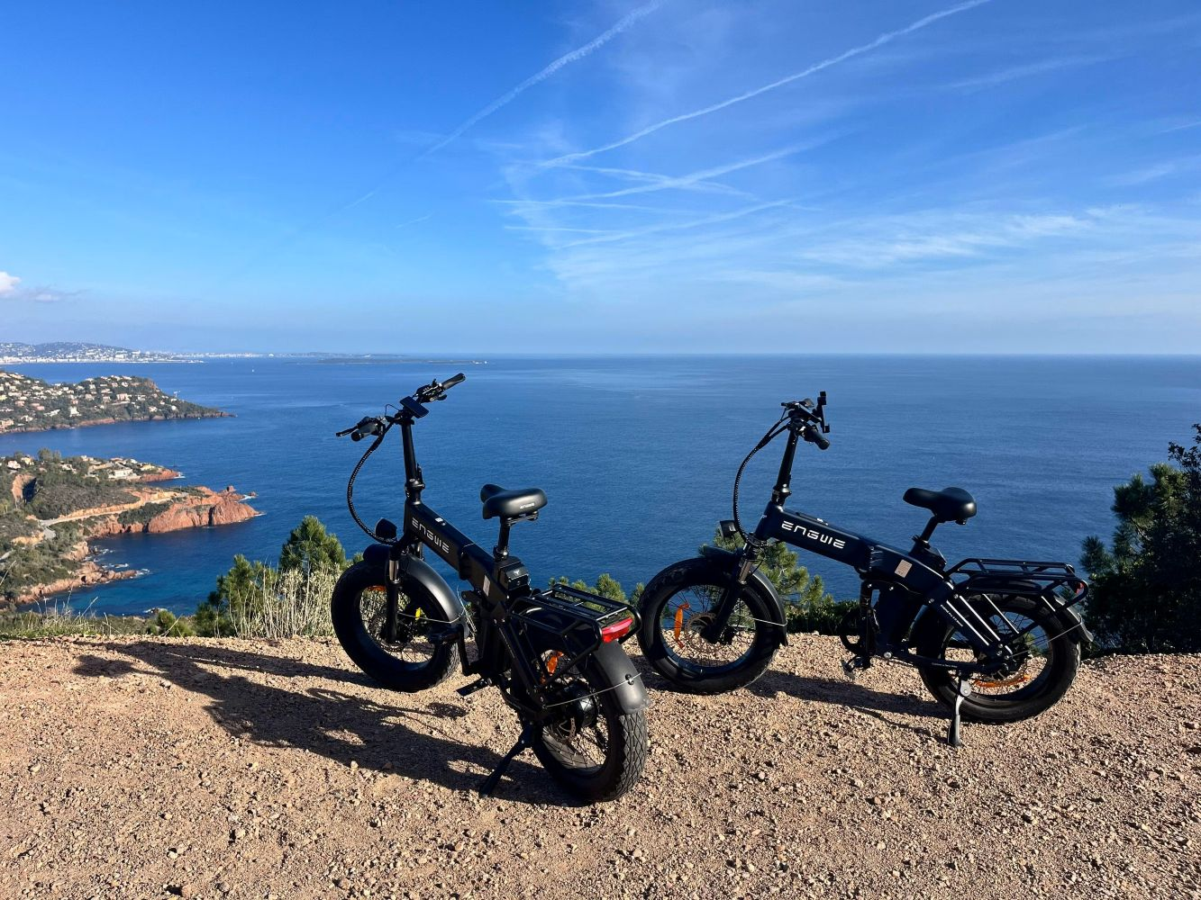 Due e-bike nere parcheggiate su un sentiero sterrato con vista sul mare.