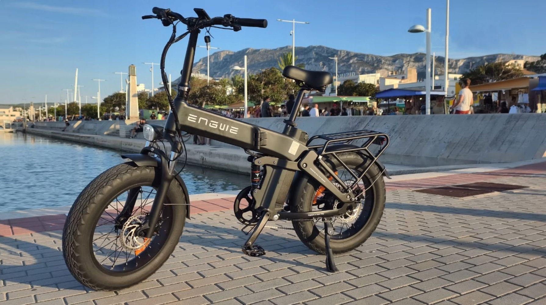 Una bicicletta elettrica nera è parcheggiata vicino all'acqua con montagne sullo sfondo.